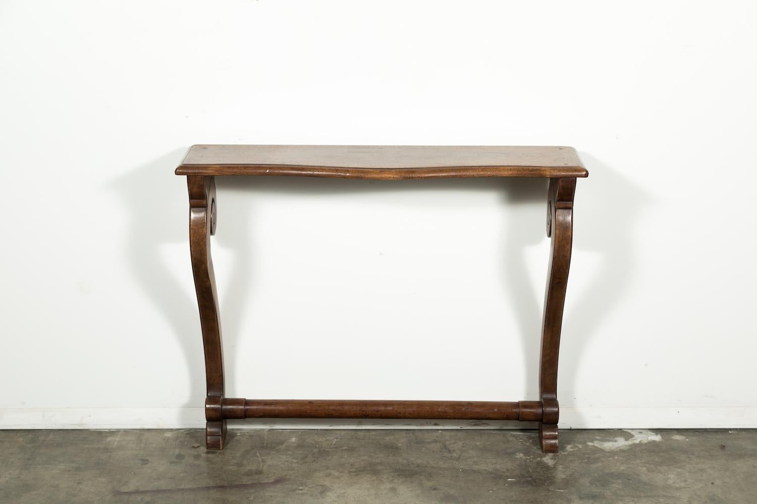 Very elegant hand carved French Empire period wall mount console supported by down-swept scrolling legs joined by a circular stretcher. The narrow depth of this console makes it a very versatile piece and its graceful curves and simplicity allow it