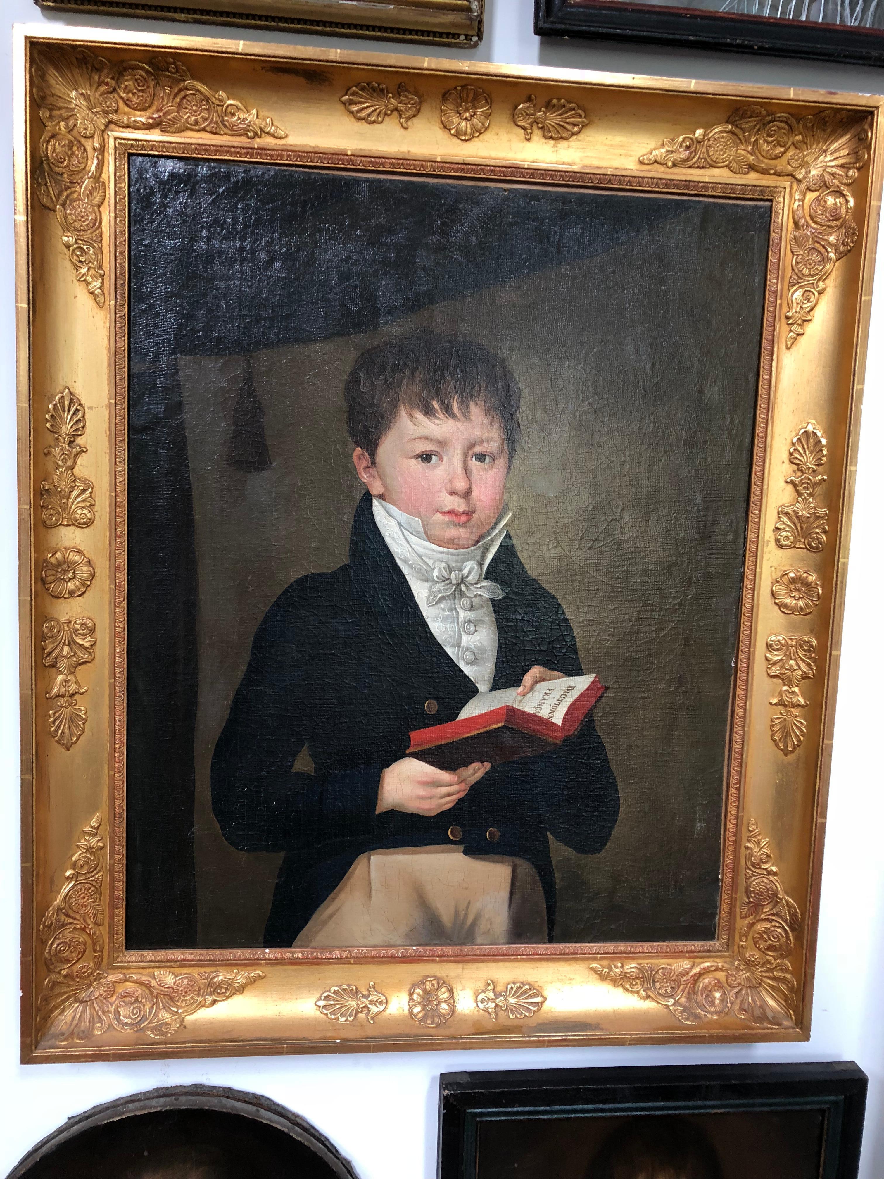 Un beau portrait grandeur nature, à l'huile sur toile, d'un jeune garçon habillé en tenue d'époque, tenant un livre intitulé 
