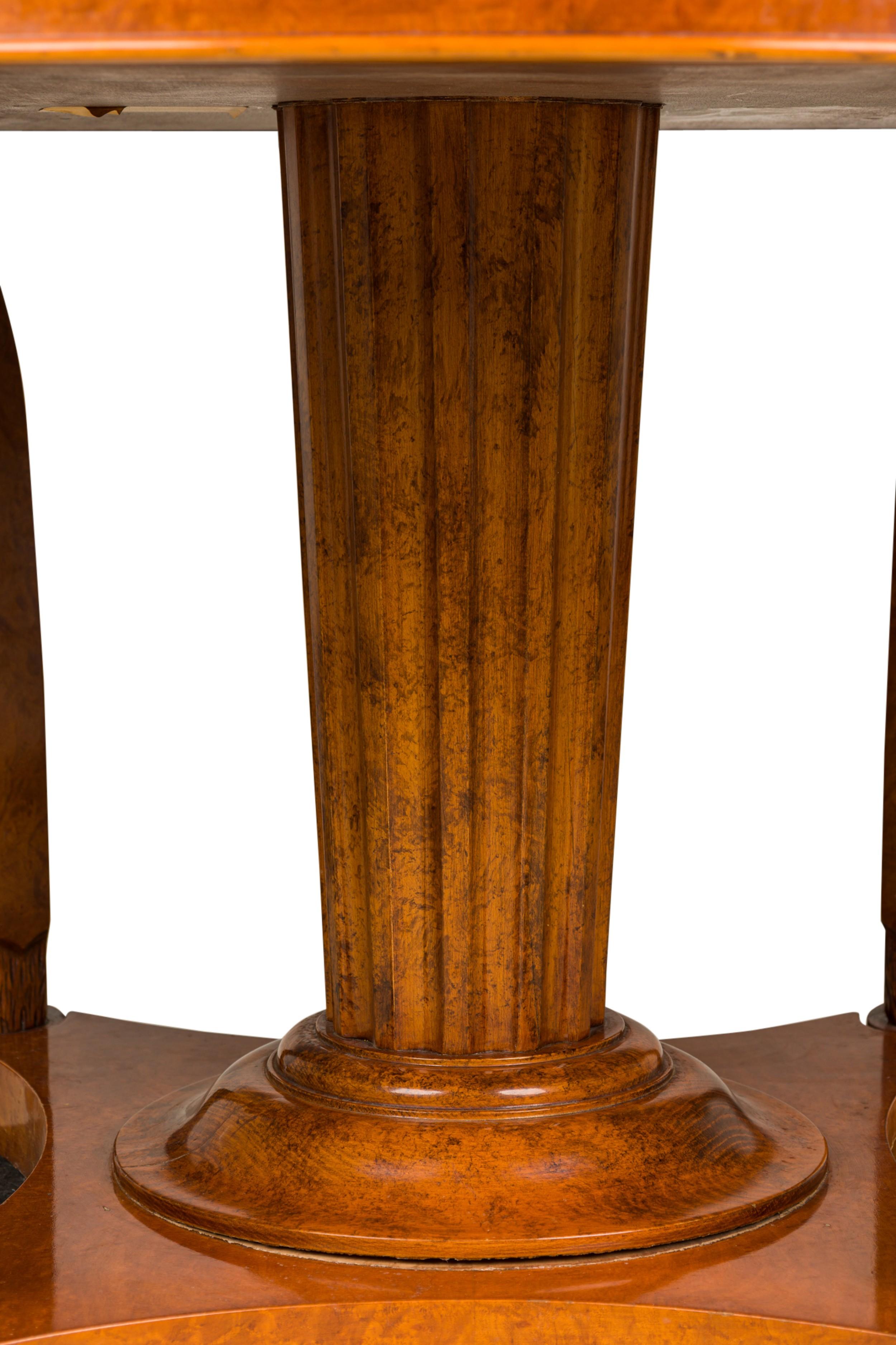 French Empire Revival-style (19/20th Century) burled walnut circular center / dining extension table which opens to accommodate 4 leaves, resting on a central fluted and tapered column flanked by four curved legs with carved lion\'s faces and ending