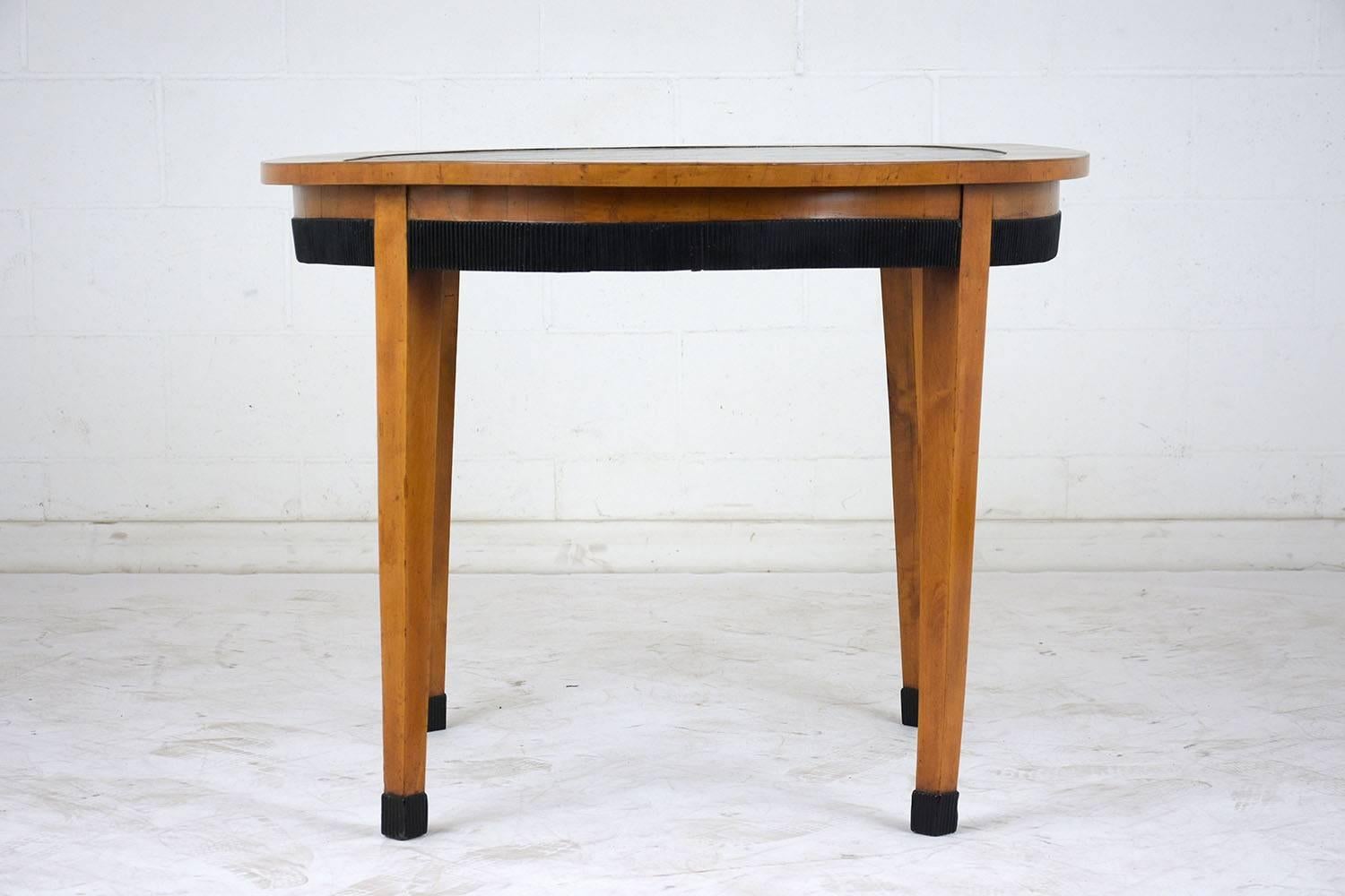 This Empire style center table is made of maple wood stained a light walnut color finish, this center table future a leather top insert with embossed gilt trim details around,  The edge of the table has an ebonized decorative moldings, The table is