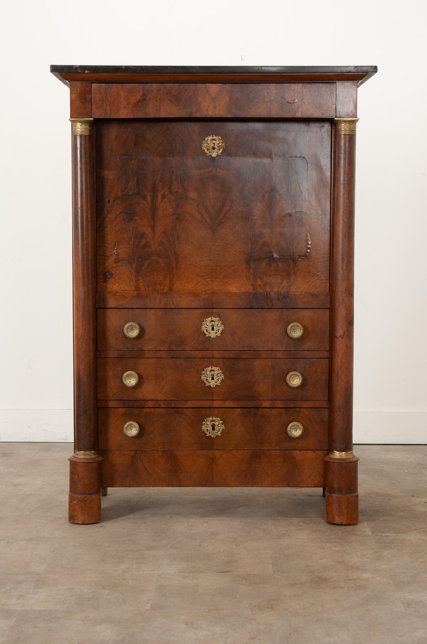 A handsome 19th century Empire secrétaire à abattant made of rich bookmatched and figured walnut. This desk has a black fossil marble top resting above a drawer, accessible with a hidden pull. Below is a fold front door revealing a fitted interior
