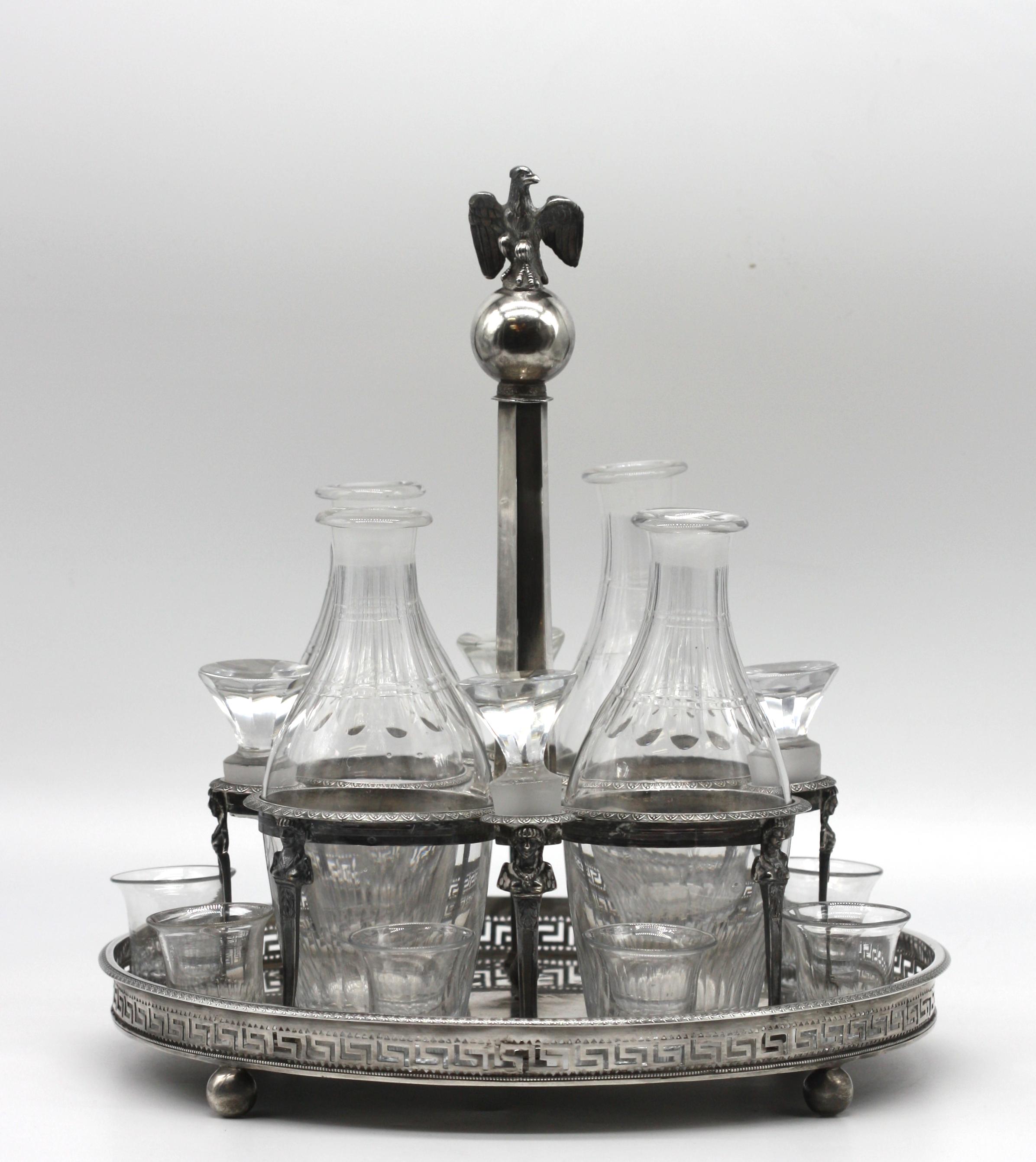 
French Empire Silver Decanter Stand, Maker Louis Joseph-Bouty, 1794-1809. 
French hallmarks. Fitted with four cut-glass bottles with stoppers and eight loose cut-glass shot glasses, (bottles and glasses possibly associated). The circular stand on
