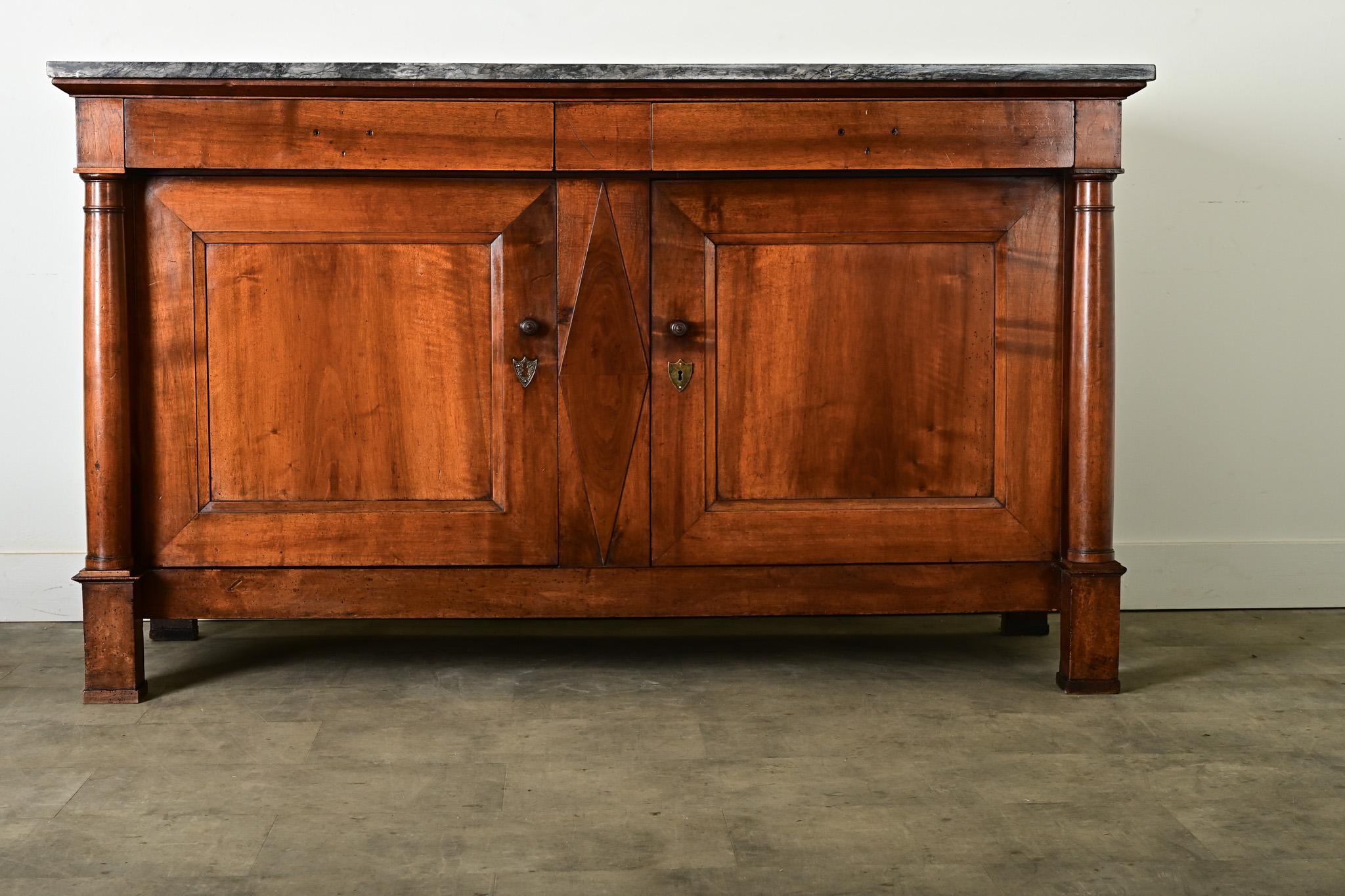 Un imponente buffet in stile Impero francese, realizzato in noce scolpito in una ricca tonalità ramata che si coordina con la superficie del piano in marmo scuro per un look classico. La pietra mostra sacche di marmorizzazione grigio scuro e greige