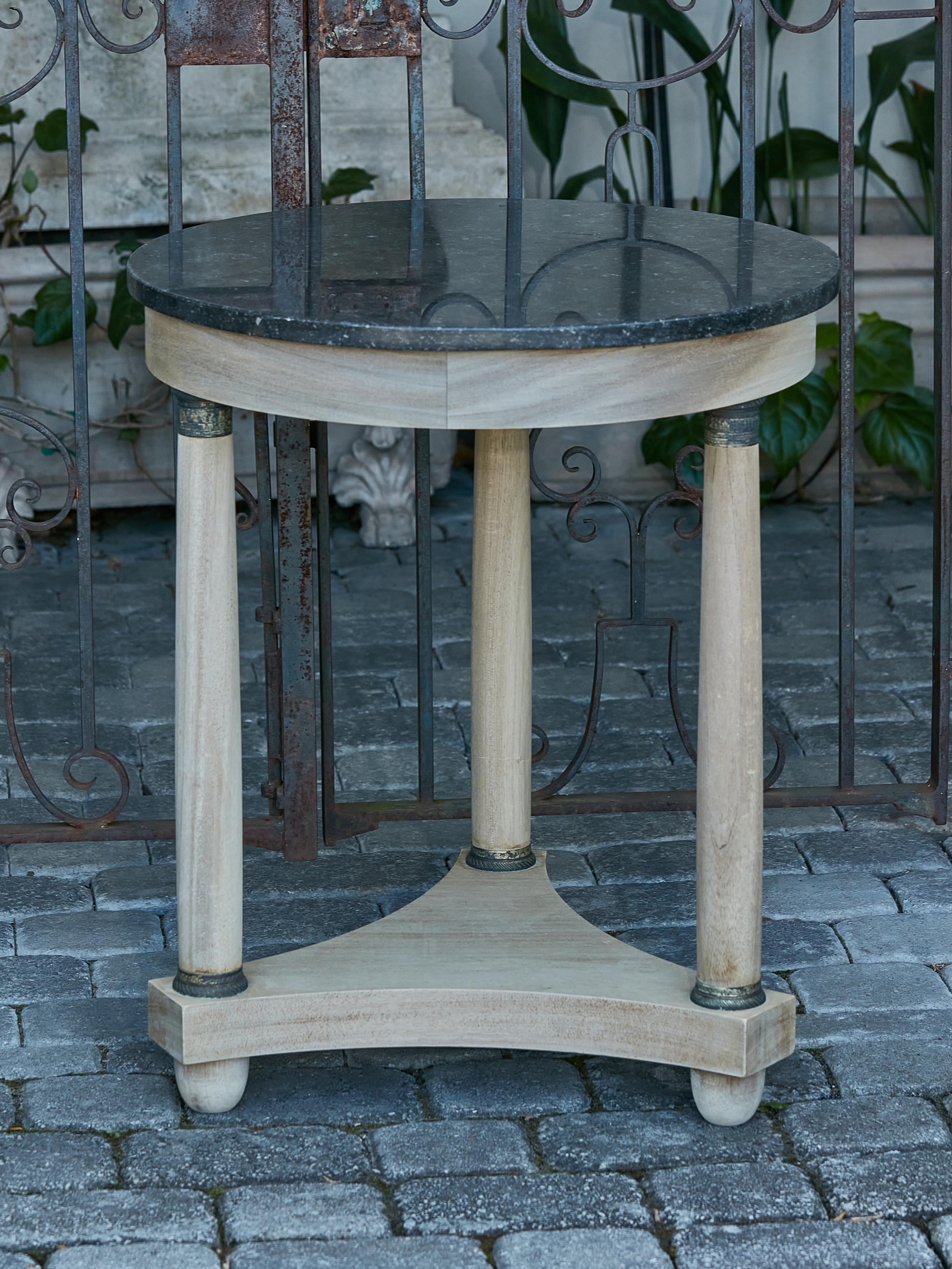 A French Empire style bleached wood side table from the 19th century with black marble top, three column legs, in-curving tripartite base and petite feet. Bask in the timeless allure of French sophistication with this 19th-century French