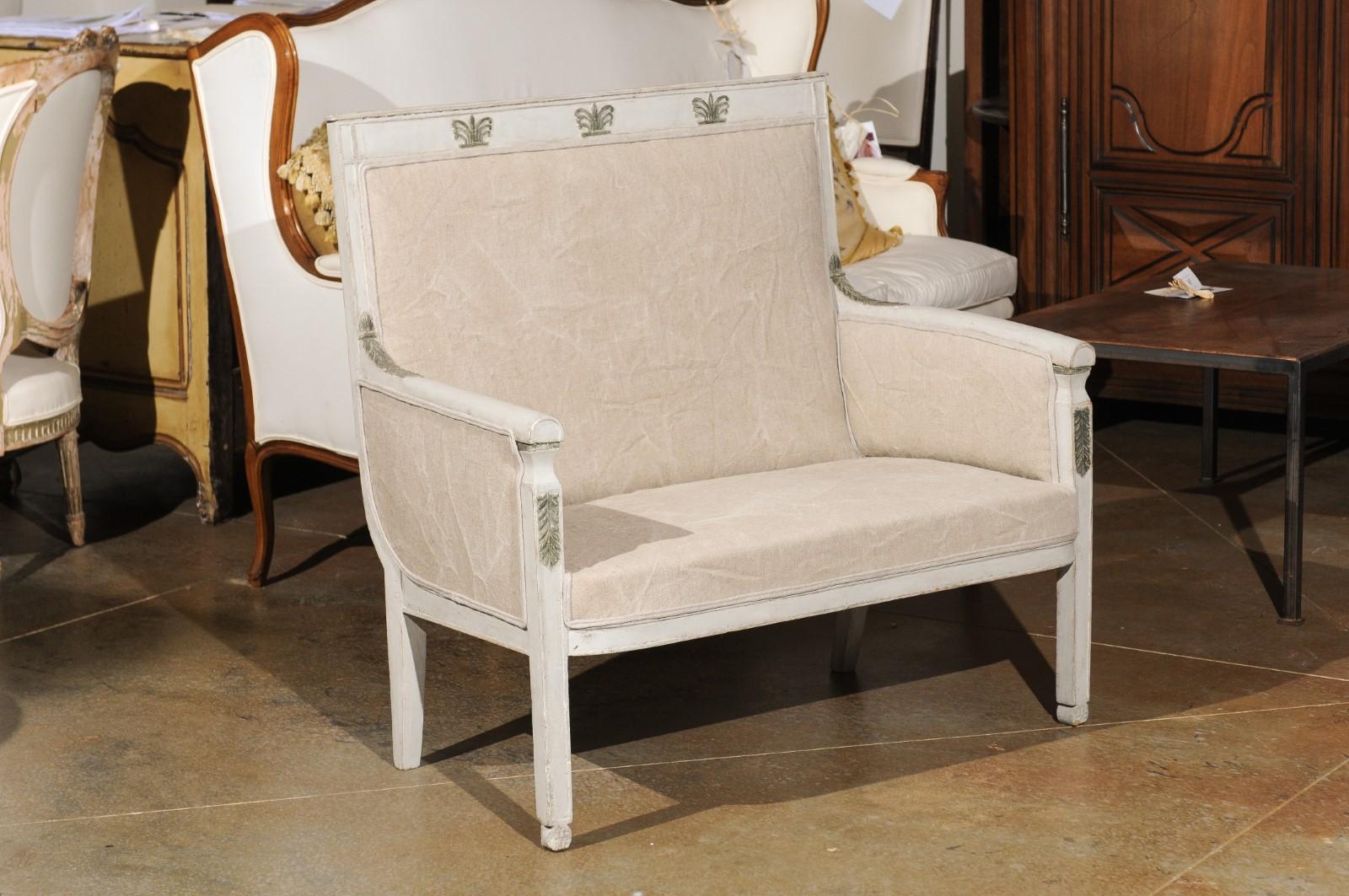 A French Empire style painted wood marquise chair from the 19th century, with carved palmettes. Born in France during the politically dynamic 19th century, this French Empire style marquise features a rectangular upholstered back, accented with