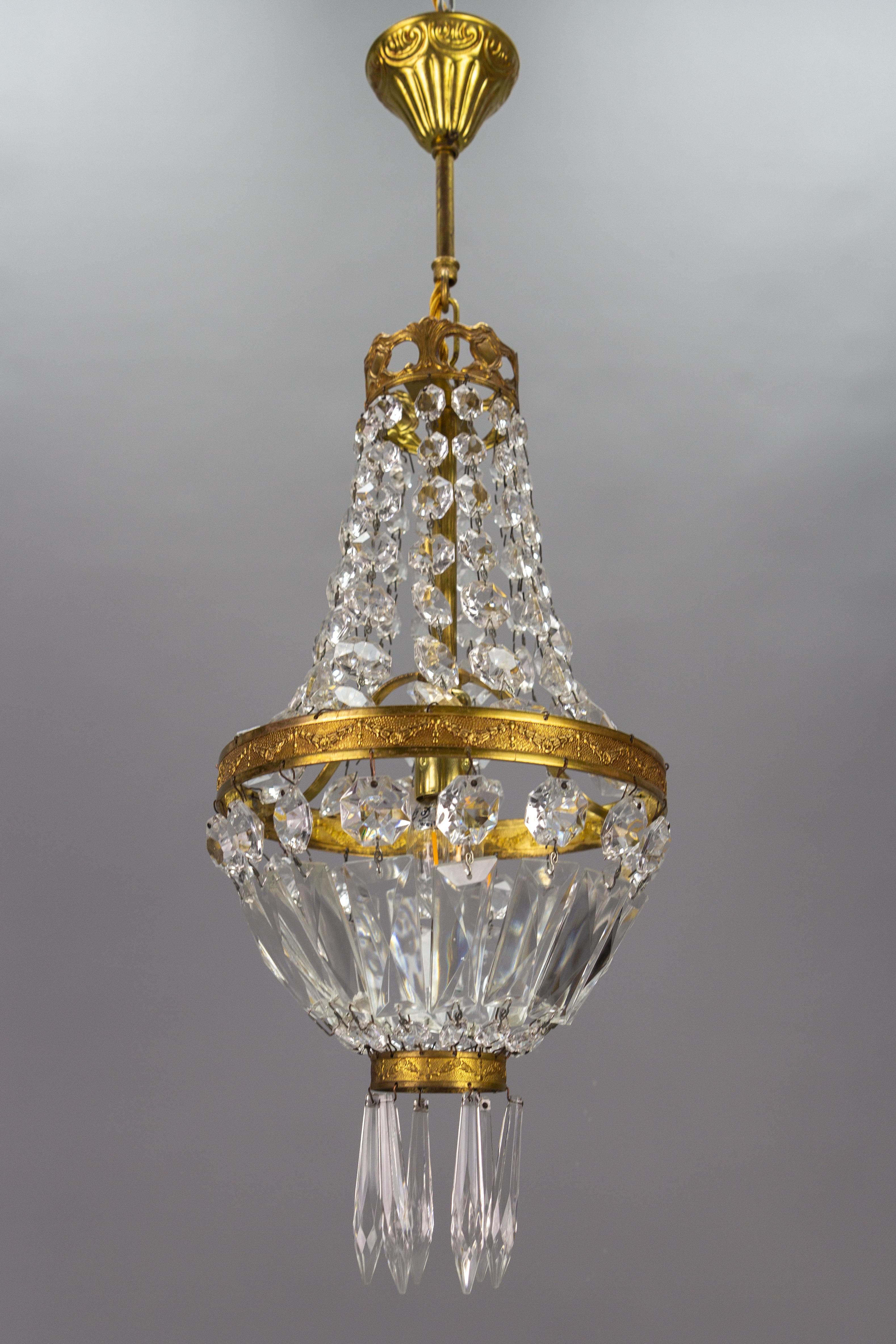 French Empire-style brass and crystal glass basket chandelier.
Charming and compact French Empire-style crystal glass and brass chandelier from the 1950s. This lovely piece has an ornate brass frame hung with chains of crystal glass beads and prisms
