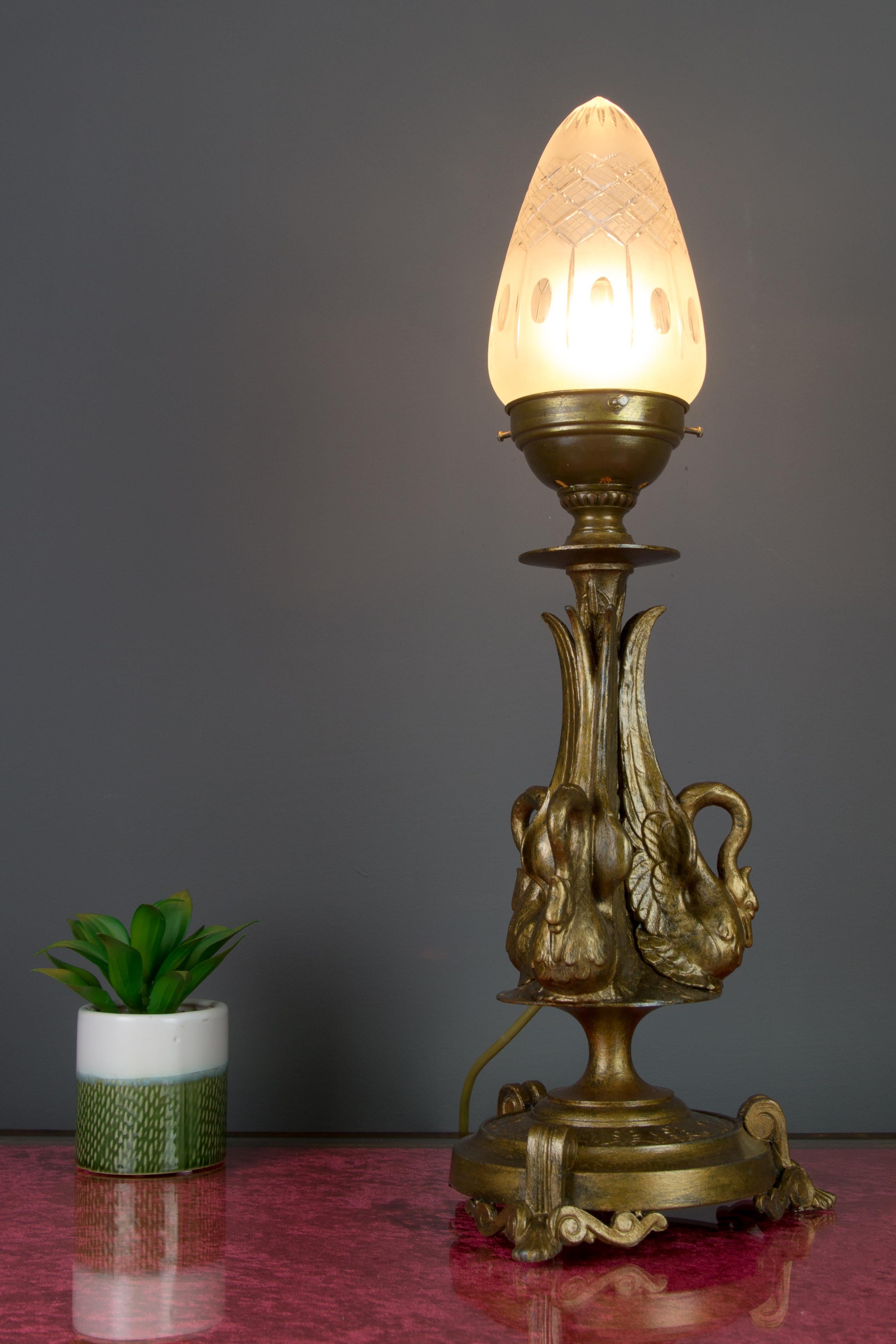 Die formschöne Tischlampe im französischen Empire-Stil, eine Petroleumlampe mit Stromanschluss, hat einen bronzefarbenen Zinnkorpus, der mit drei eleganten Schwanenfiguren verziert ist. Eine Fassung für Glühbirnen der Größe E27 (E26). In die USA