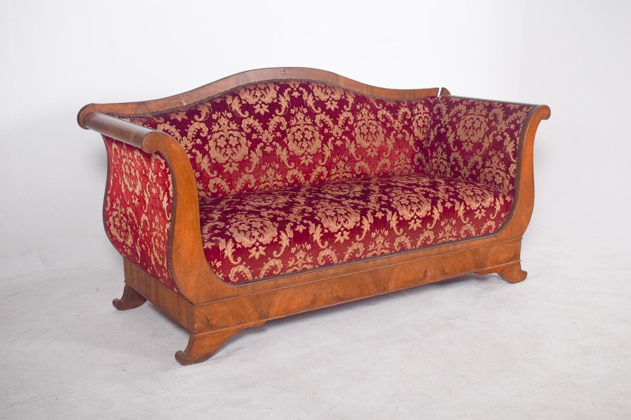 Empire-style canapé, upholstered in red fabric. Characterized by its sturdy structure in light-toned wood with a varnished finish, contrasting with the rich, detailed upholstery.
The deep red upholstery with gold floral pattern is a real visual
