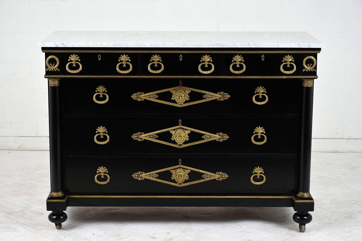 This 1900s French Empire-style chest of drawers is made of mahogany wood with an ebonized and lacquered finish. On top of the chest is a white with gray veins marble slab with a flat polish. The six drawers are adorned with decorative brass hardware