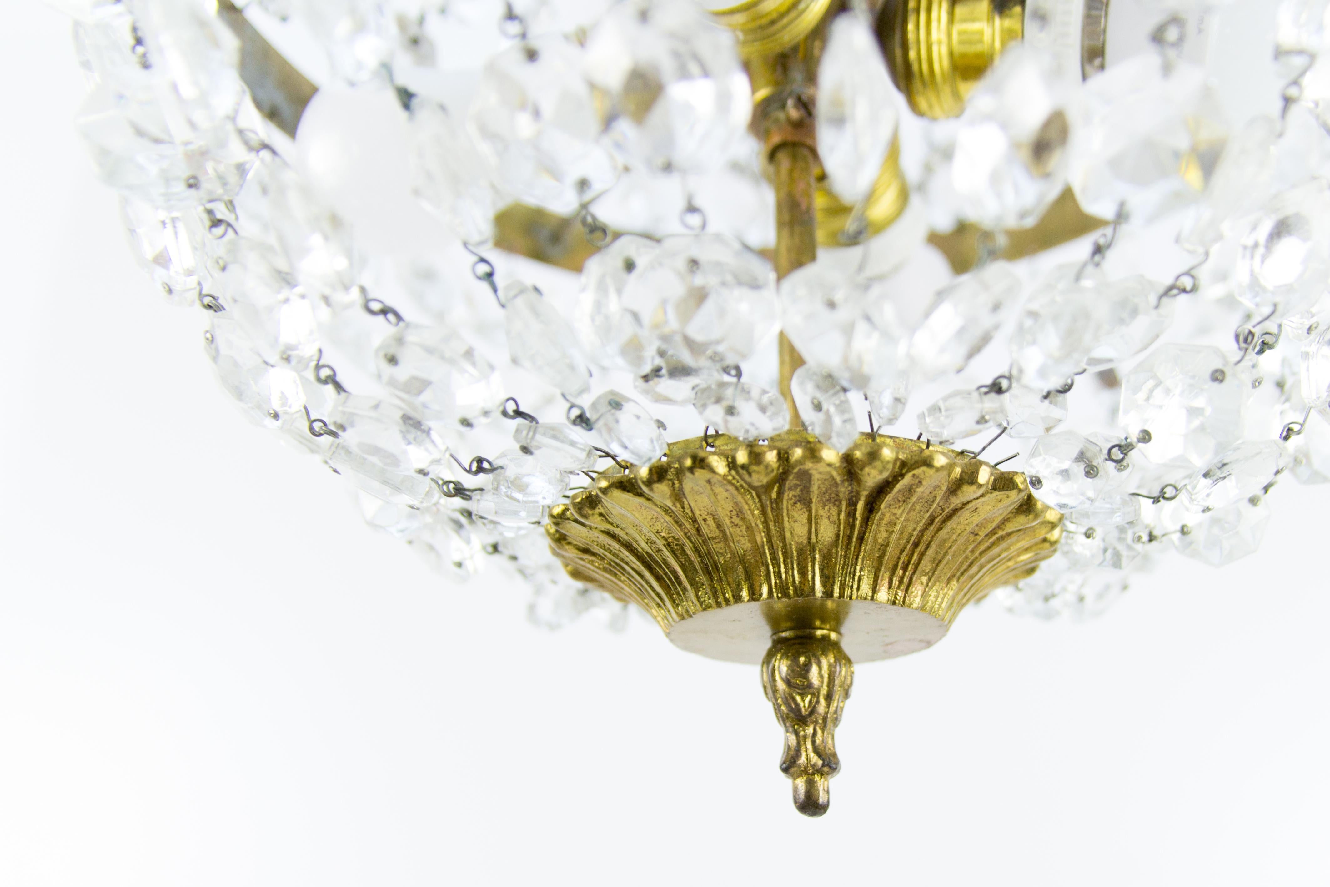 French Empire style four-light crystal, brass, and bronze basket-shaped chandelier from the 1920s. Four interior lights with original E27 (E26) size light bulb sockets. The crown is decorated with bronze plumes and pendeloque crystal