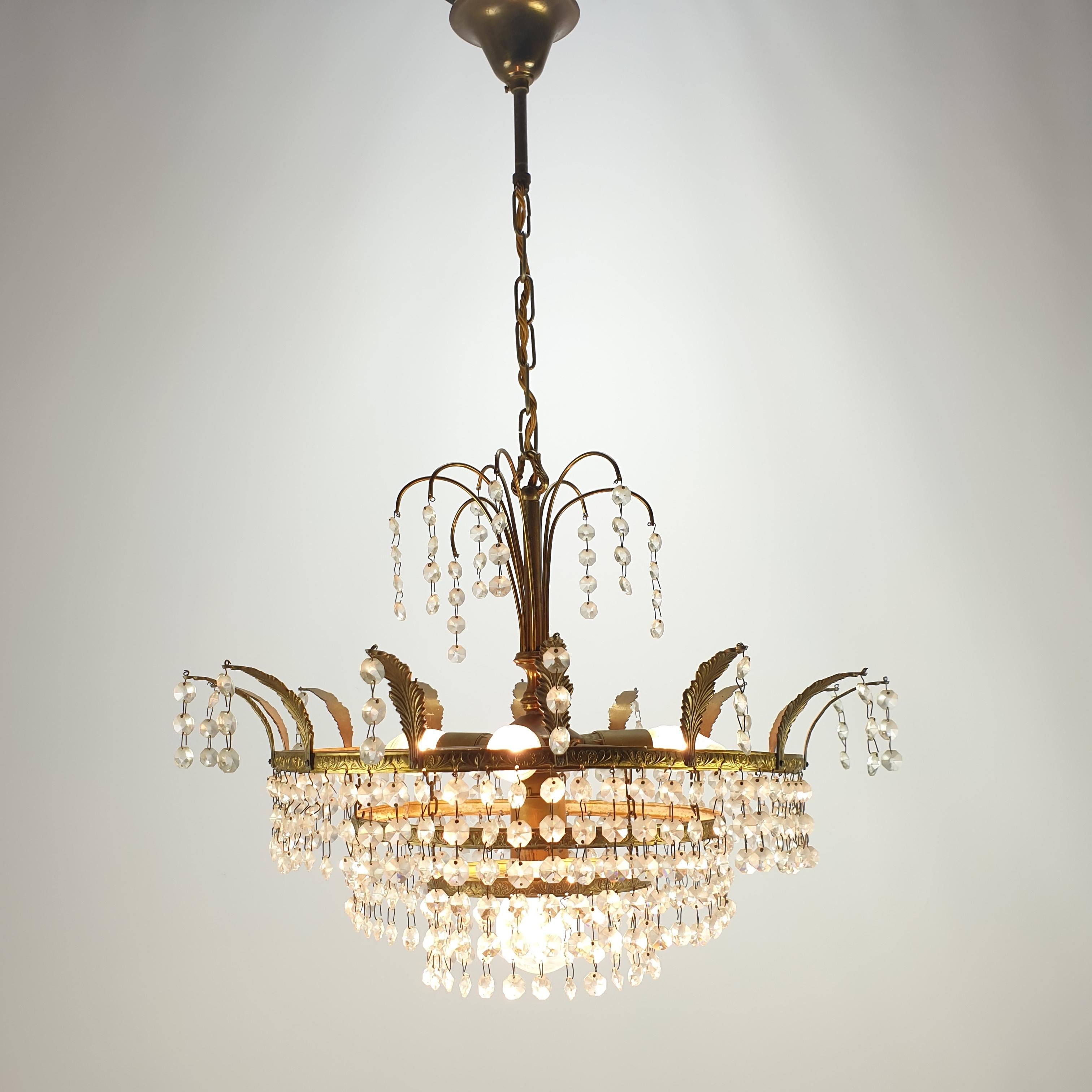 Charming French Empire-style crystal glass and brass chandelier from the 1920s.

This lovely piece has an ornate bronze frame hung with prisms of crystal glass. 
The crystal glass prisms create a sparkling effect and reflect elegance which is sure