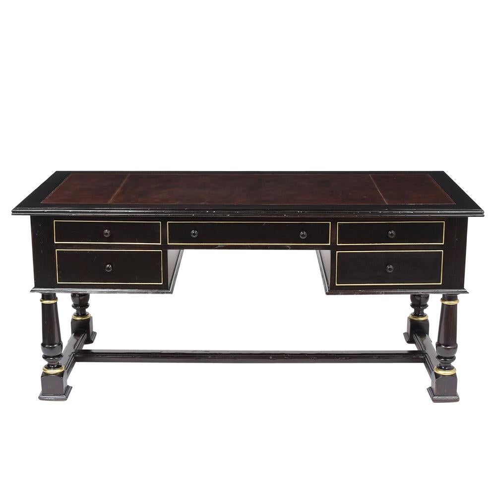 This French Empire desk has been fully restored, is made out of mahogany wood stained in a newly ebonized lacquered finish with gilt molding details and newly restored. This desk also features a faux leather top dyed in burgundy color with embossed
