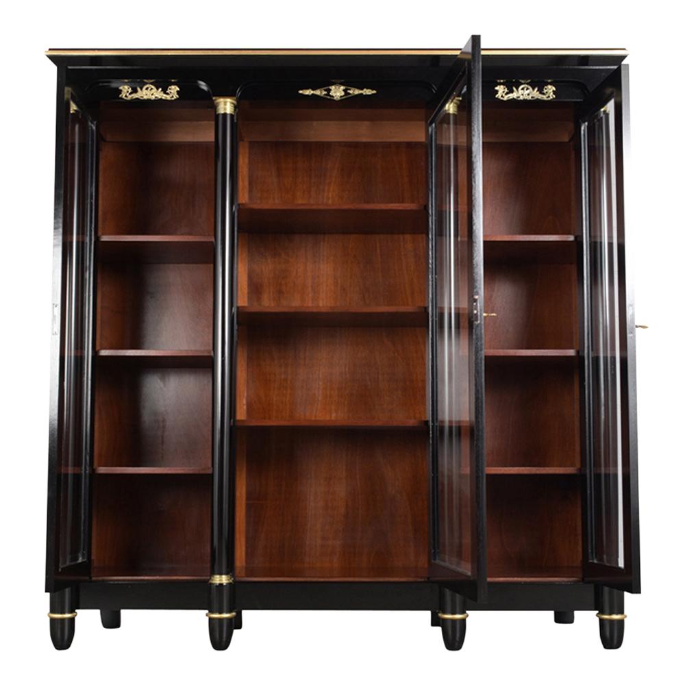This French Empire style bookcase is fully restored, made out of mahogany wood, and has been stained a rich ebonized color with a newly lacquered finish. This bookcase has an arched top four carved wood columns with gilt capitals brass accents