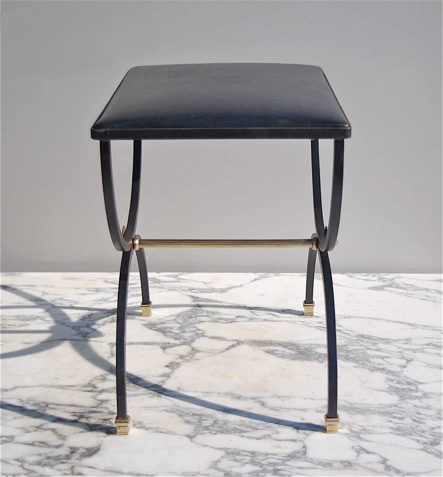 French Empire, neoclassical style ottoman or X-shaped foot stool. It has a curvilinear X-frame form made from black lacquered metal resting on brass square feet. It has a central fluted, tubular brass support with round finials at each end.