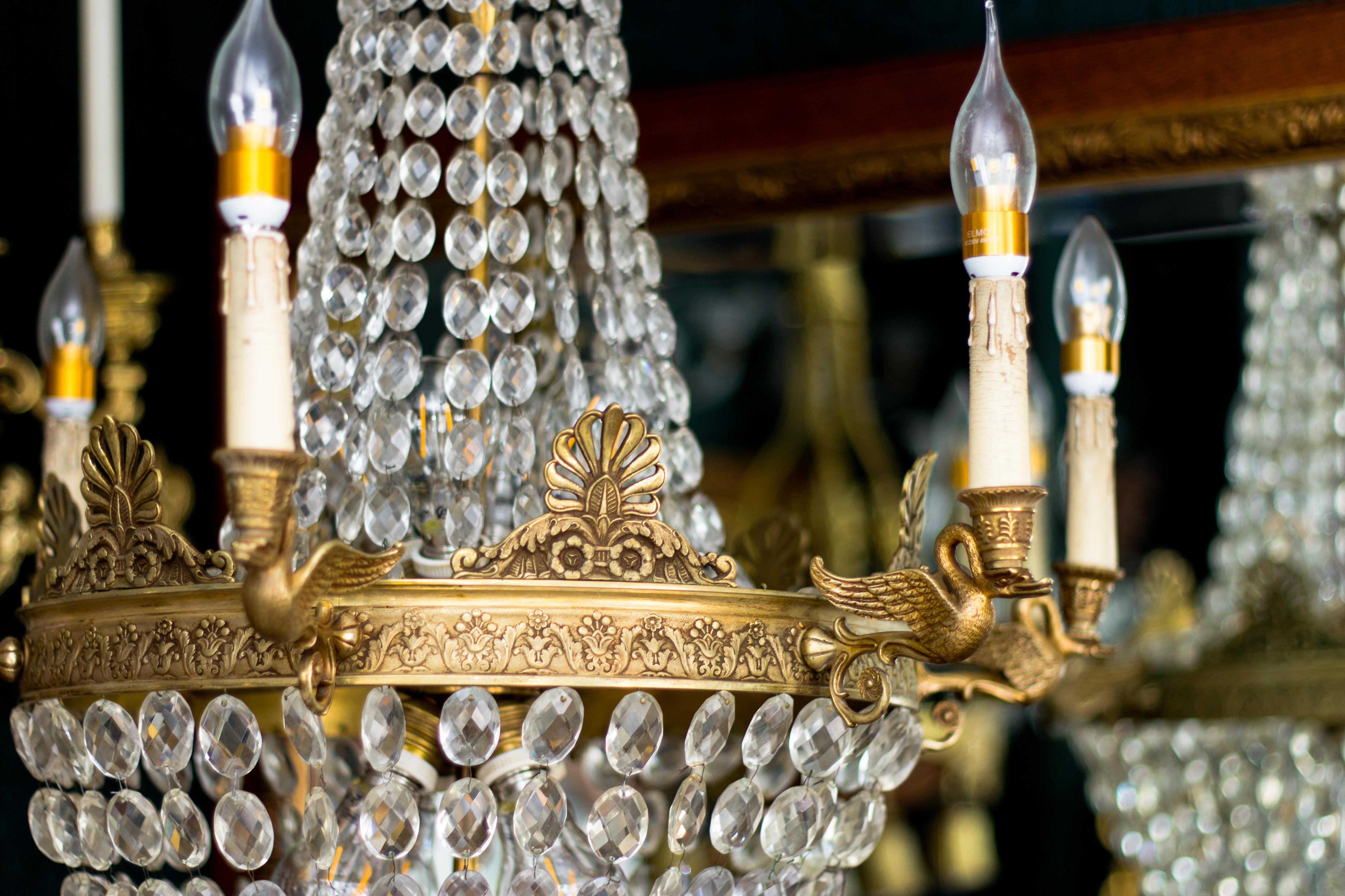 French Empire style crystal and bronze basket chandelier with six bronze swan arms; bronze plume castings adorn the top of the chandelier and around the ring for the basket, decorated with foliate and floral decors.
Each bronze swan arm has an E14