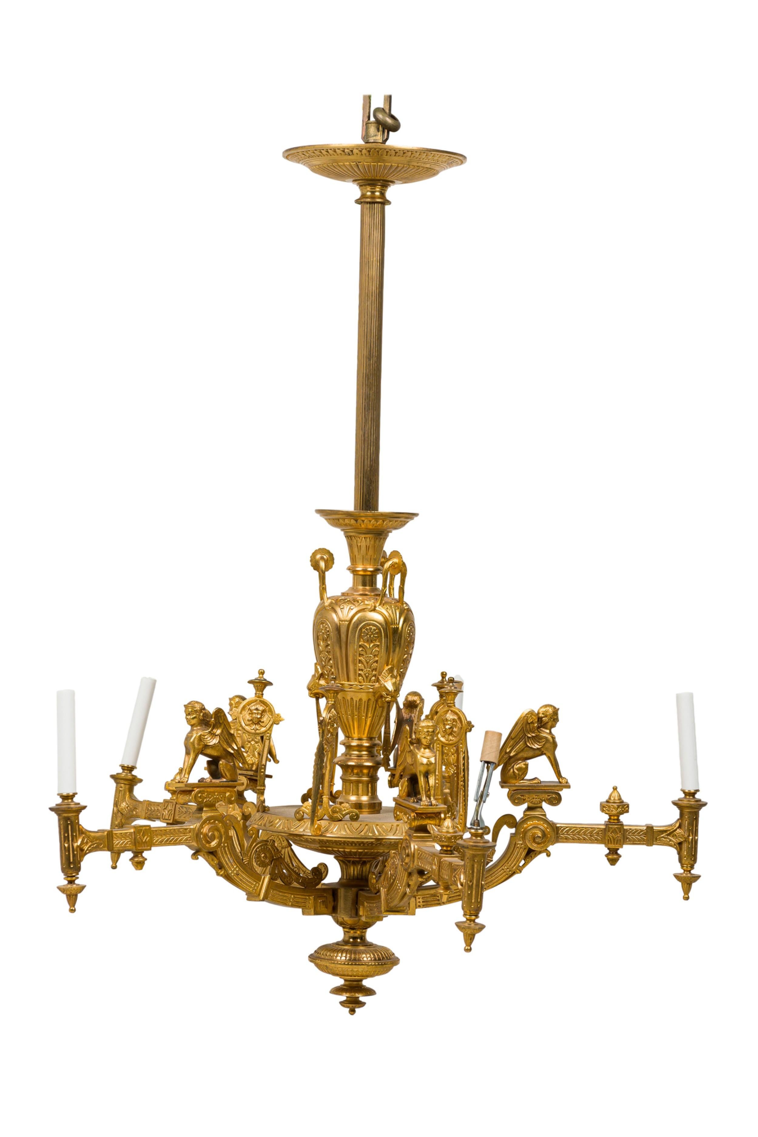 Lampadario a 5 luci in bronzo dorato in stile Impero francese (1880) di forma neoclassica con figure di sfingi, urne antiche, teste di medaglioni e riserve a più motivi.

