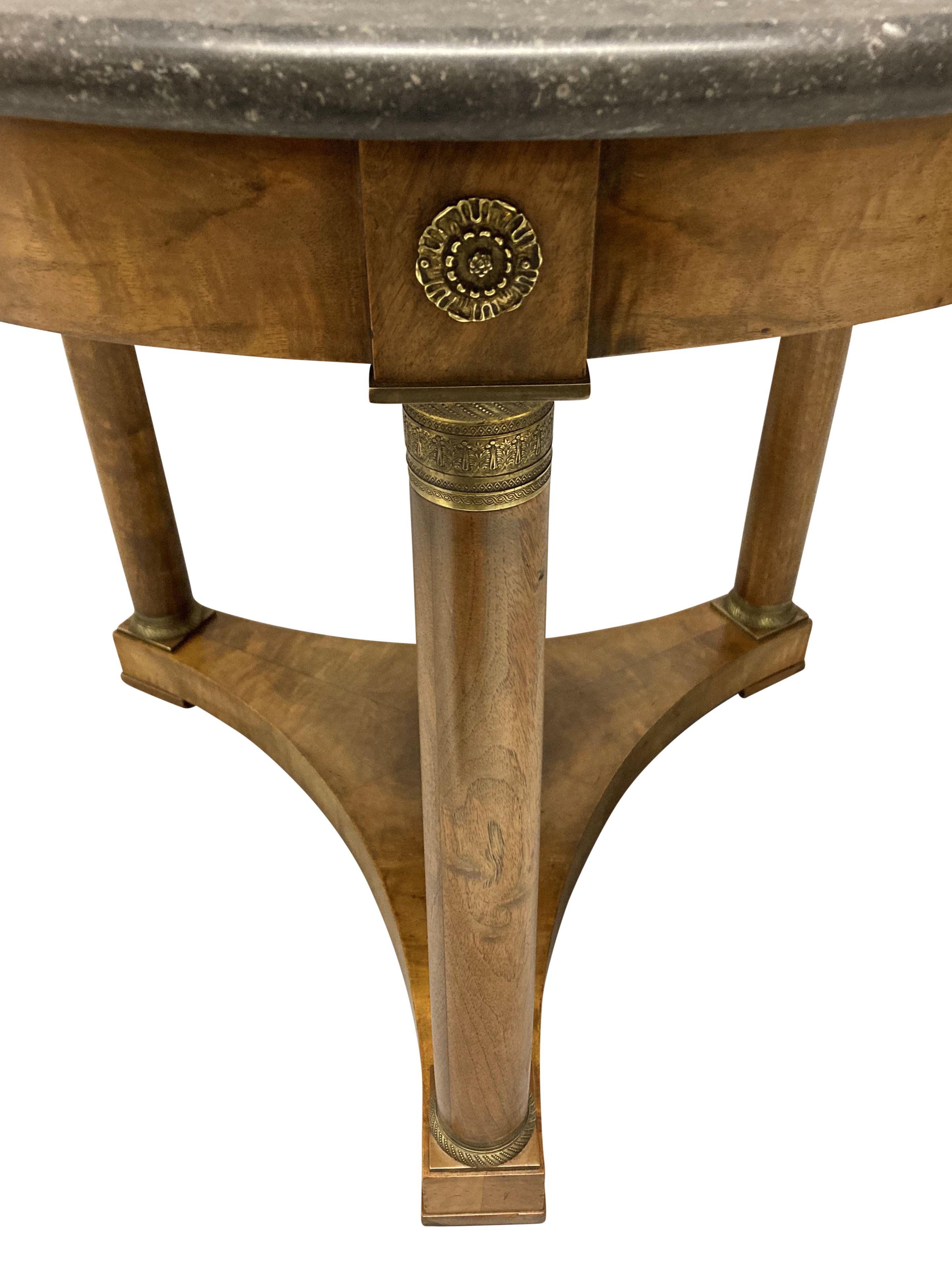 A French Empire style gueridon table in faded mahogany, with brass mounts and a grey marble top.