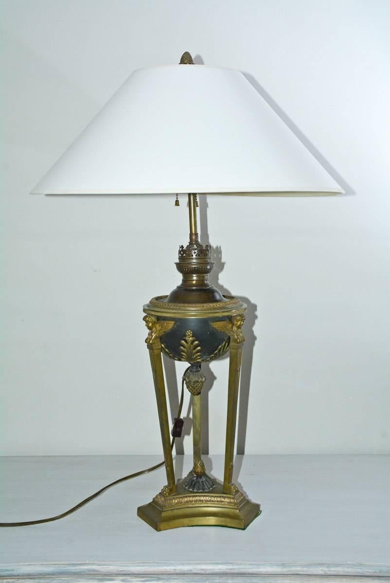 Ultra elegant classical Empire style dark green tôle with oil reservoir encircled by bronze band raised on cloven hoof tripod feet over incurved base. Once an oil lamp later converted to two lite table lamp, with white parchment coolie shape lamp
