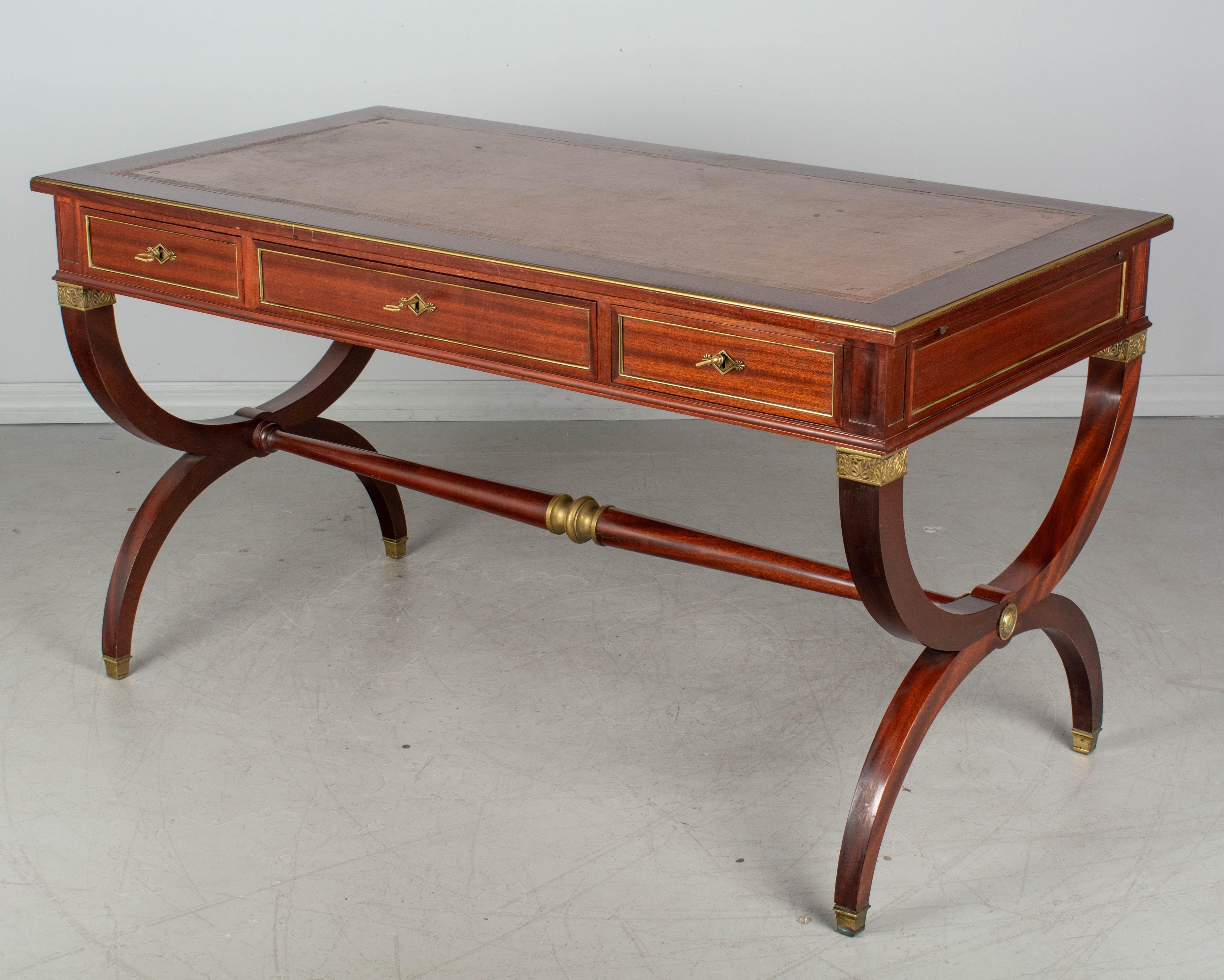 A French Empire style mahogany desk with leather top. Pullout / pull-out extensions on both sides provide additional work surface. Three dovetailed drawers with working locks and three keys. Brass hardware, trim and decorative medallions. Turned