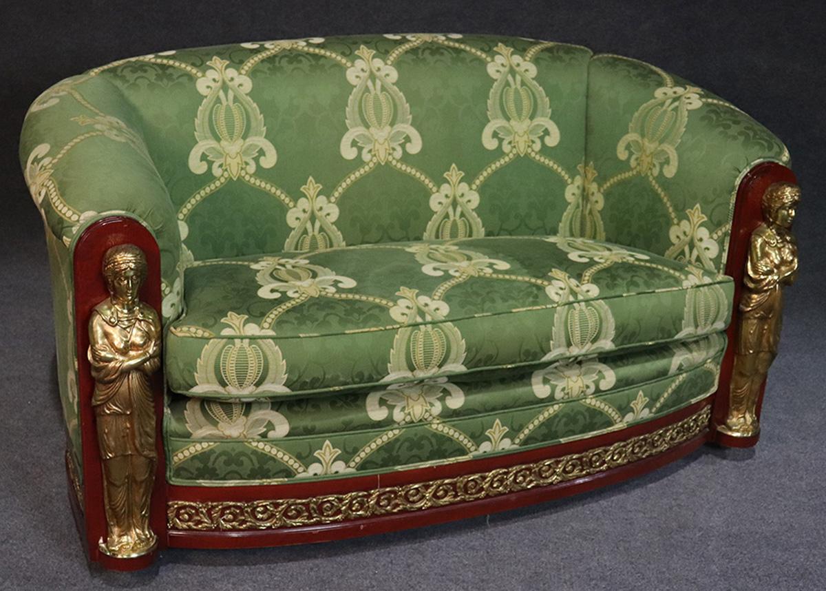 This is a gorgeous French Empire sofa settee with fantastic solid brass figures at each end. This beautiful piece dates to the 1950s era and has beautiful green upholstery and cast brass ormolu on the bottom. The settee sits on large spherical