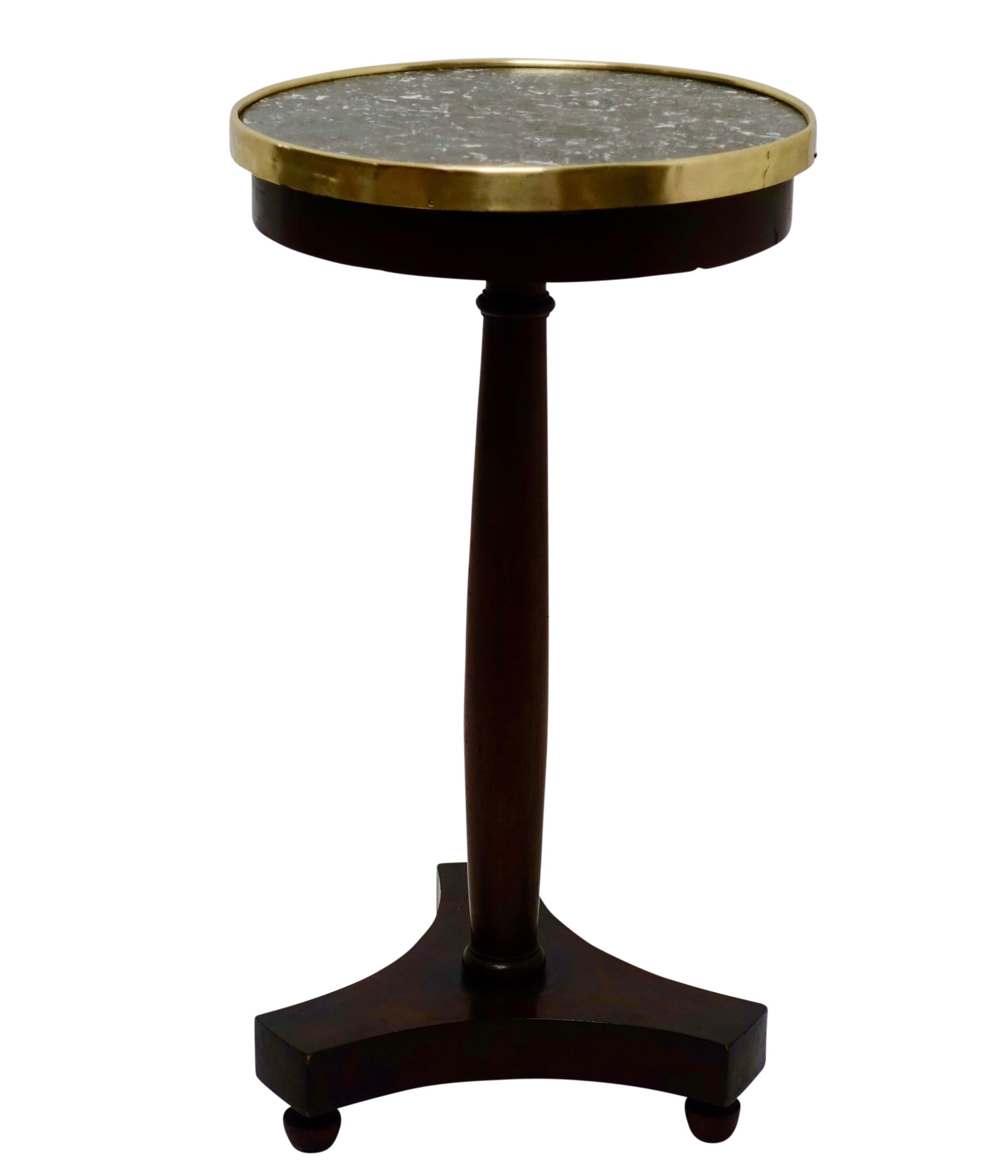 A unique Empire style mahogany side table or candle stand with an inset gray marble top and brass gallery, supported on a shaped column fixed to tripartite base sitting on acorn shape feet, France, circa 1840.