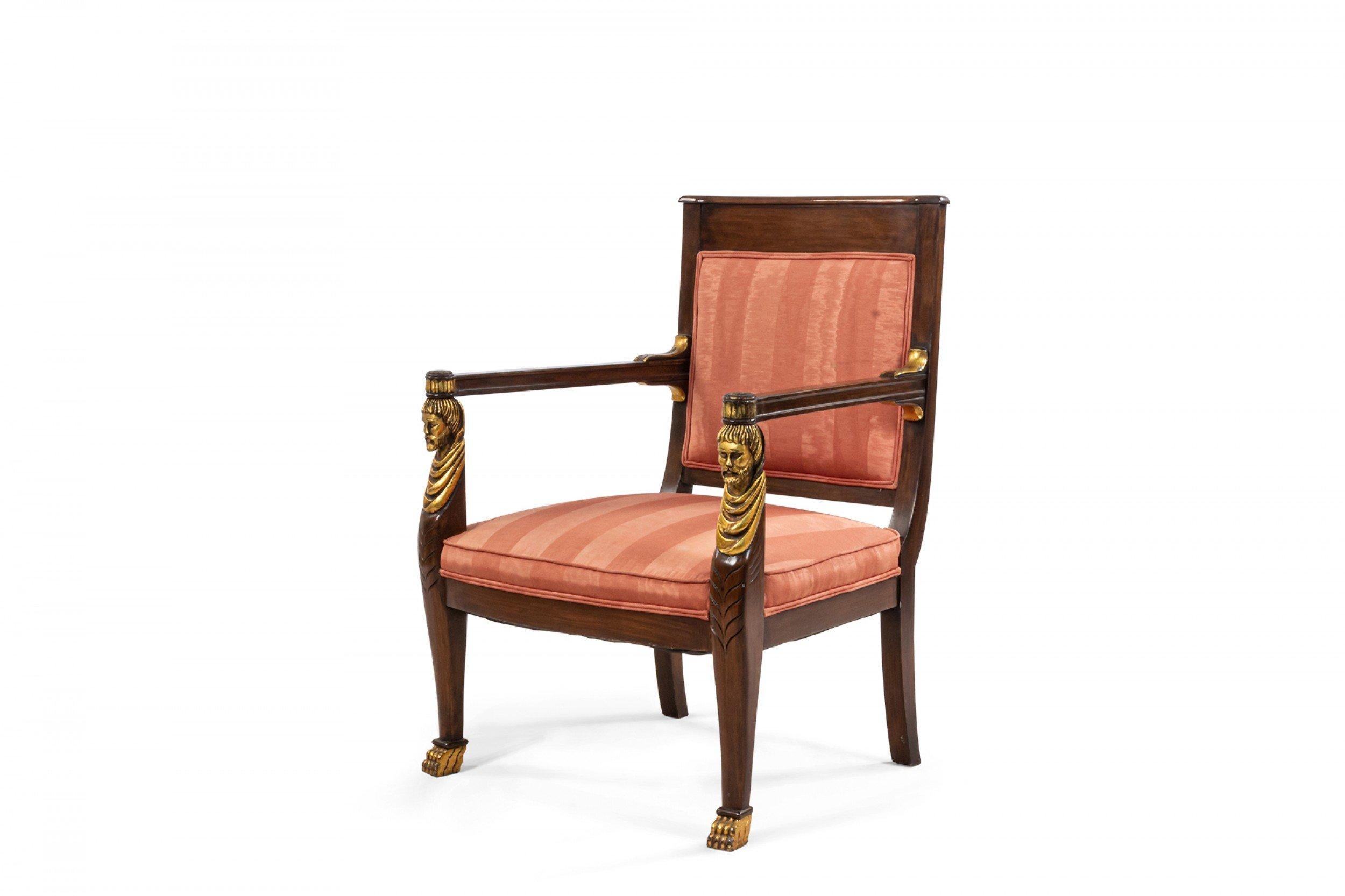 Paire de fauteuils de style Empire français (20e siècle) en acajou avec pieds dorés et détails de têtes sculptées classiques sur les bras et tapisserie rayée rose.