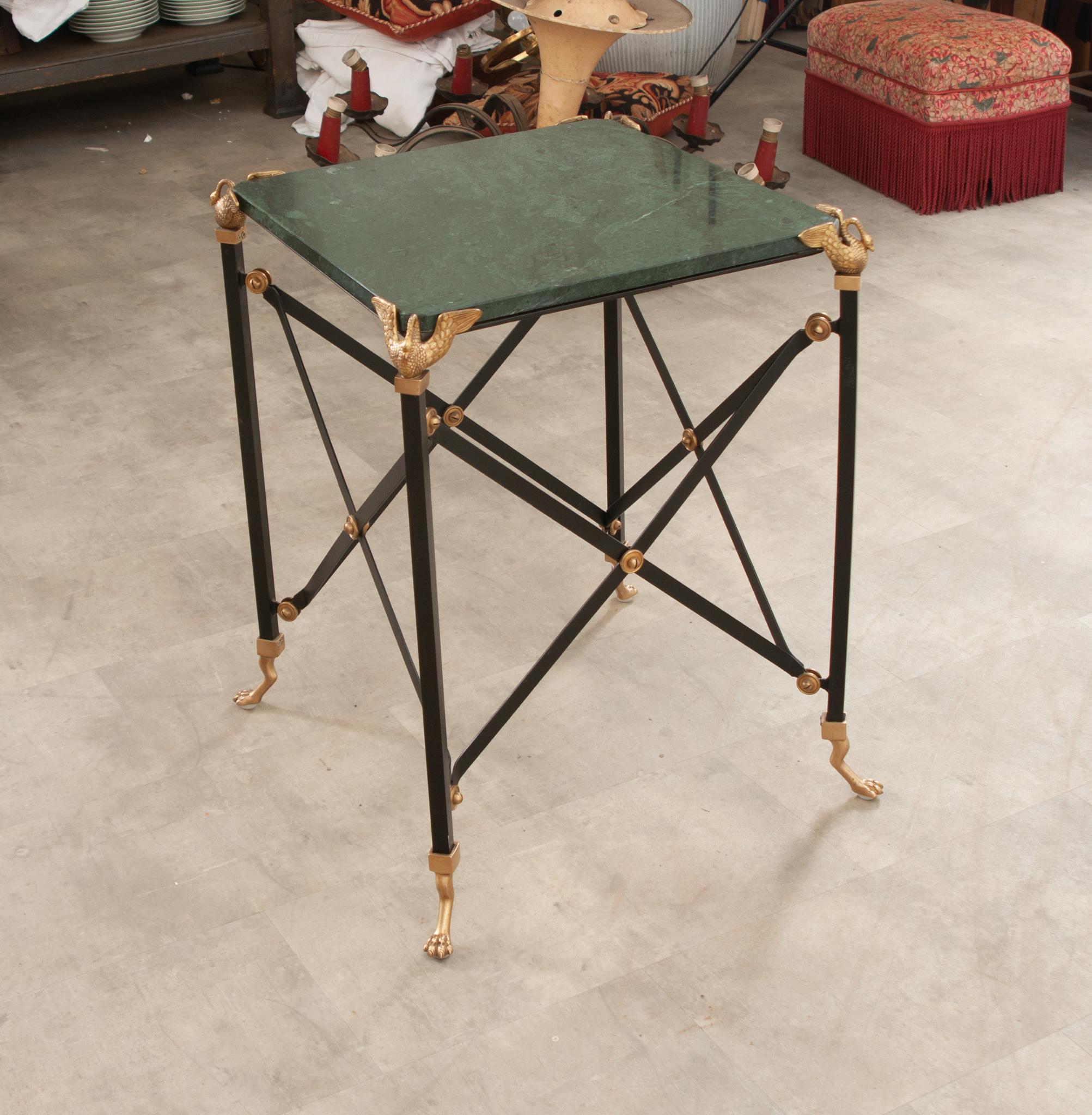 A vintage Empire style side table handcrafted in France. A wonderful square piece of emerald green marble featuring black veining and hazy white patterns sits atop a cast iron base with elongated legs topped with brass open wing swans and ending in