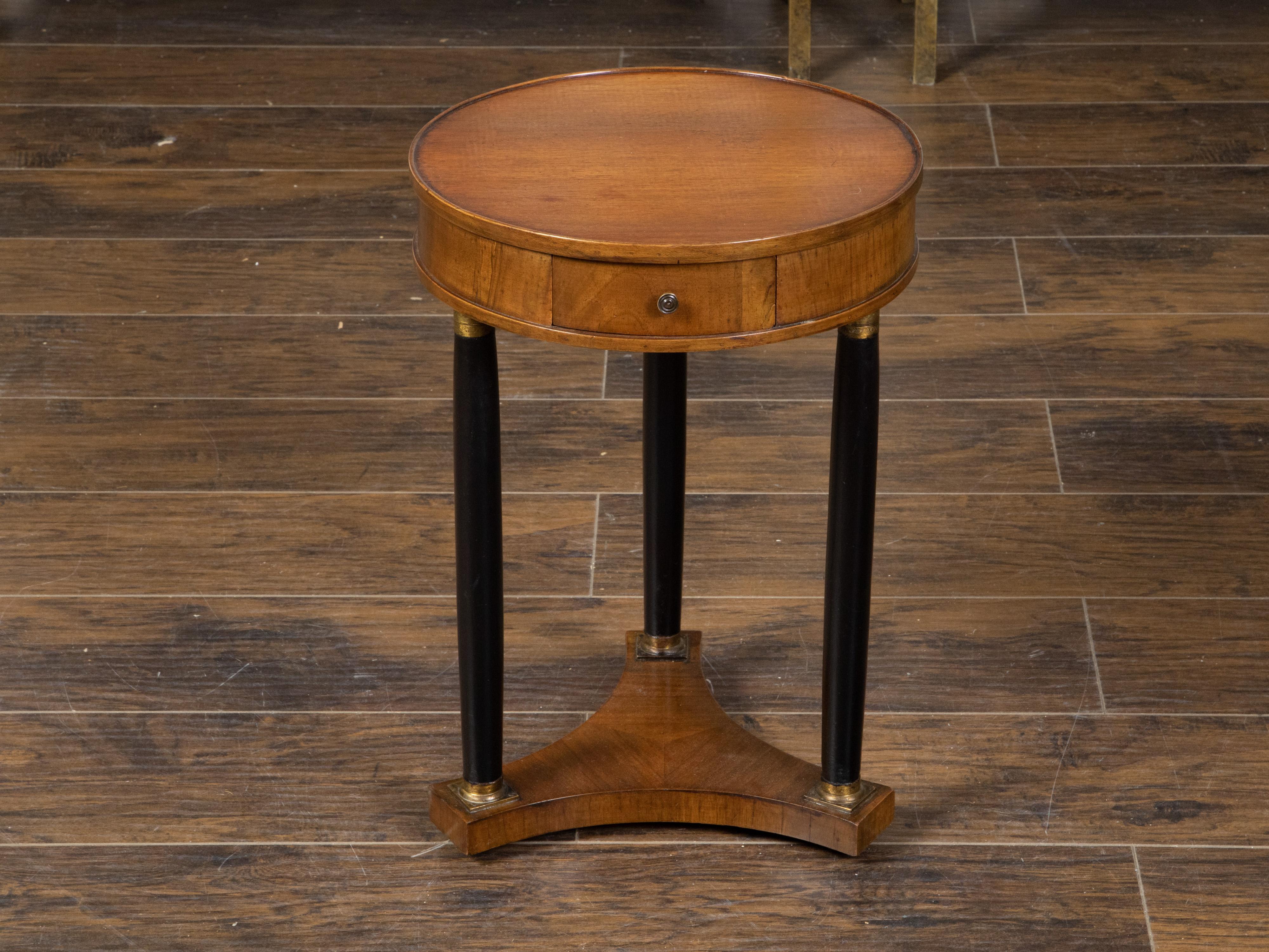 A French Empire style walnut drinks table from the mid 20th century, with ebonized columns and bronze mounts. Created in France during the Midcentury period, this walnut Empire style drinks table features a circular top sitting above a simple apron