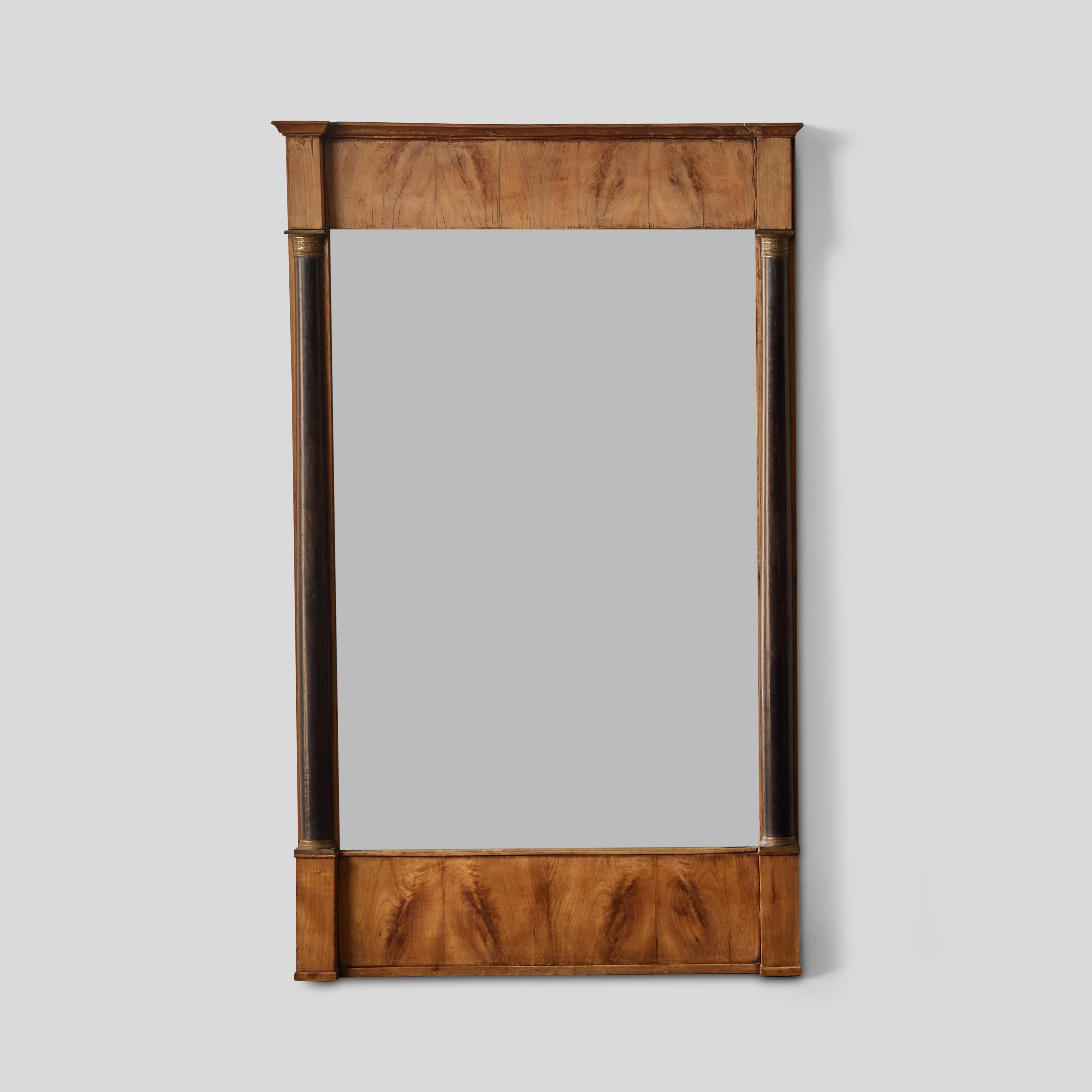 French Empire style mirror from the 1820s, featuring two slim Ionic ebonized columns, honey-toned burled wood and a restrained architectural schema. Simple and refined, the piece has an almost proto-Modern feel. 

France, circa 1820.

Measures: