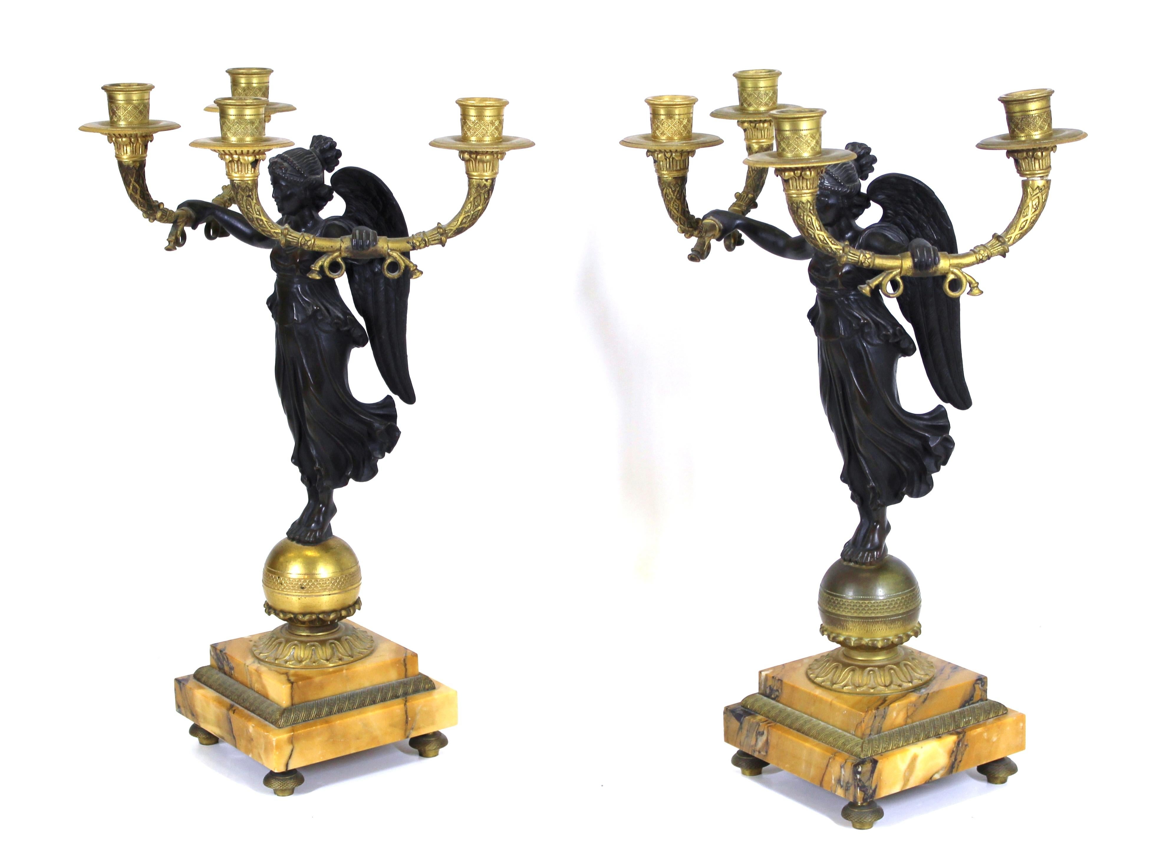 French Empire style bronze dore and patinated bronze pair of candelabras with winged victories on stepped marble bases holding up two candle holders on each side, circa mid-19th century.