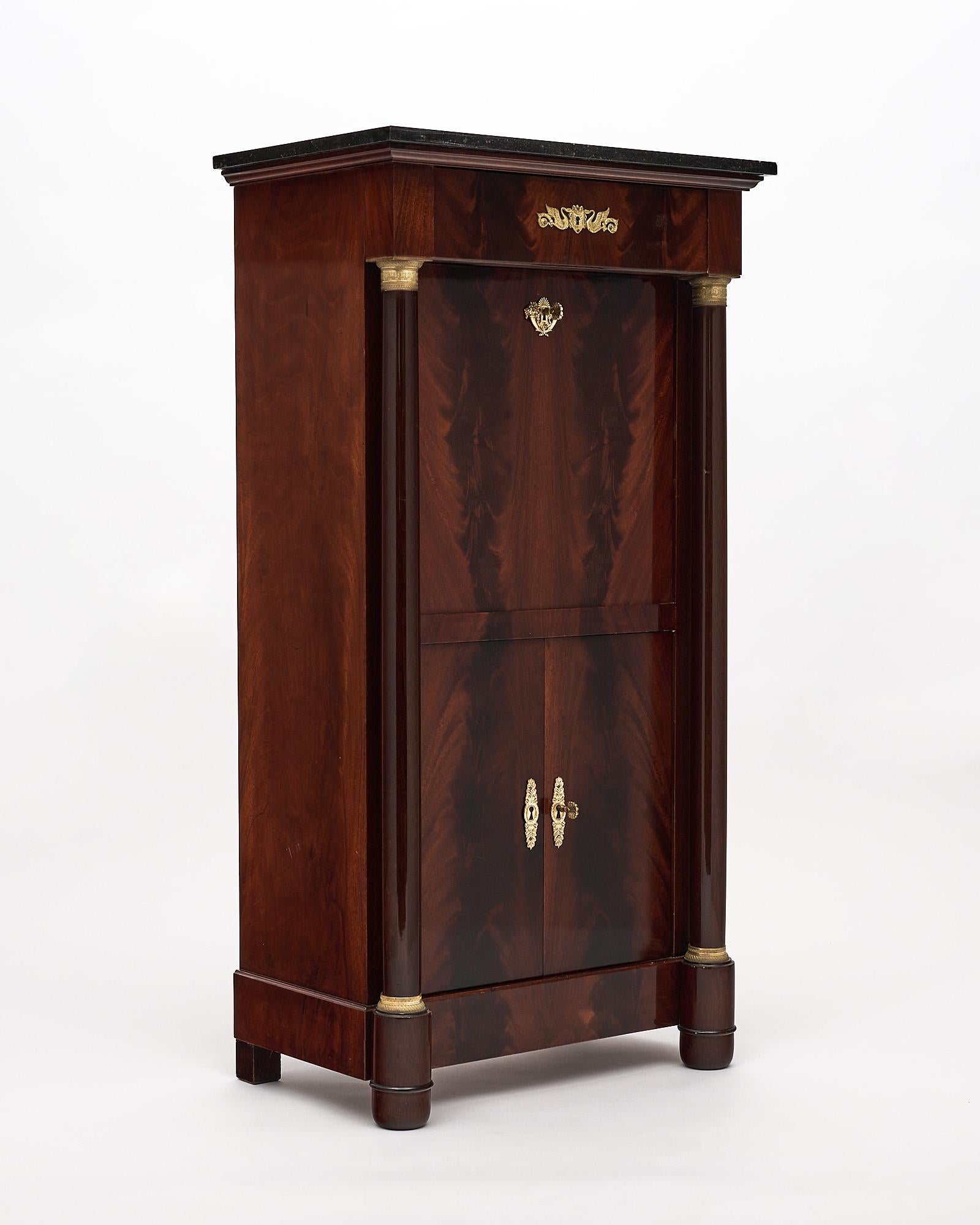 Secretary, French, in the Empire style and made of Cuban flamed Mahogany, finished in a Museum quality French polish. The exquisite cabinet boasts two detached columns with finely cast bronzes throughout. The drop front opens to an original red