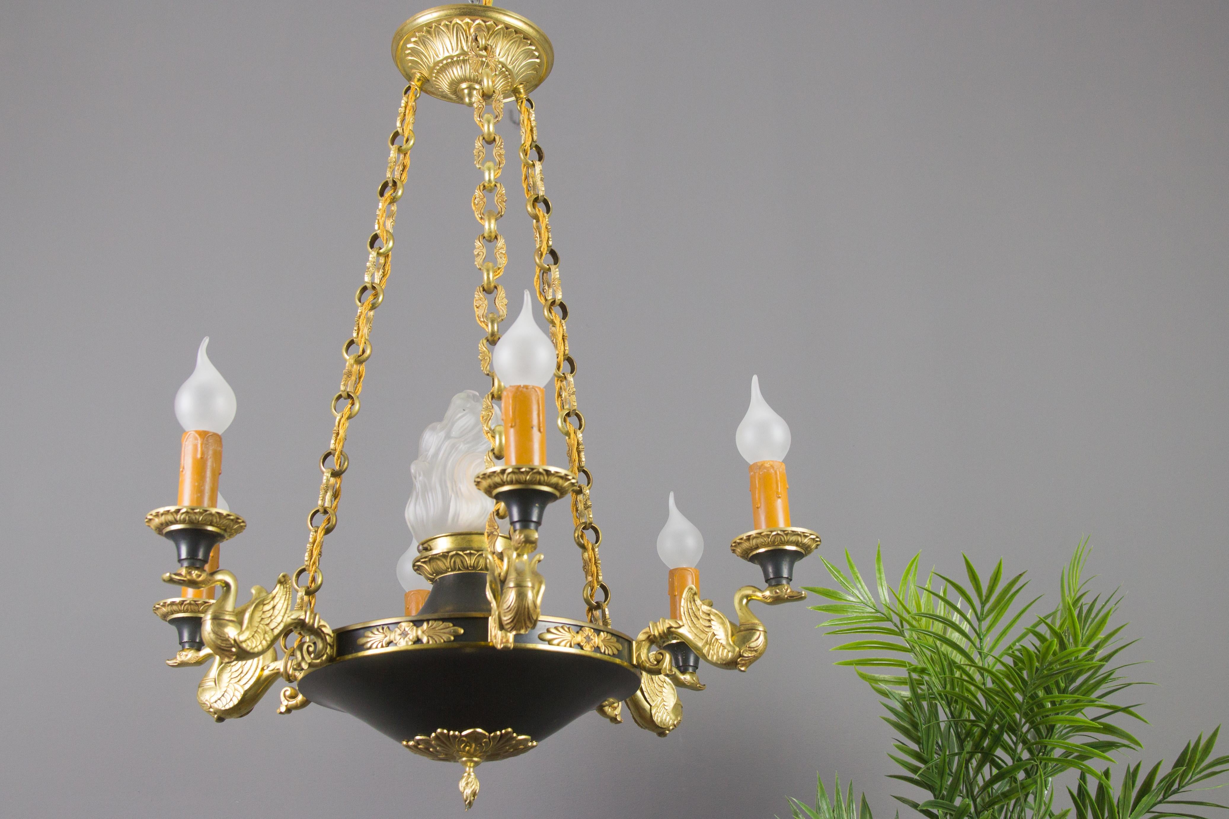 This beautiful French Empire-style chandelier features six bronze swan arms. Dark green painted body with decorative bronze mounts and richly ornate pine finial, on top centered with flame torch glass shade. Impressive and very decorative