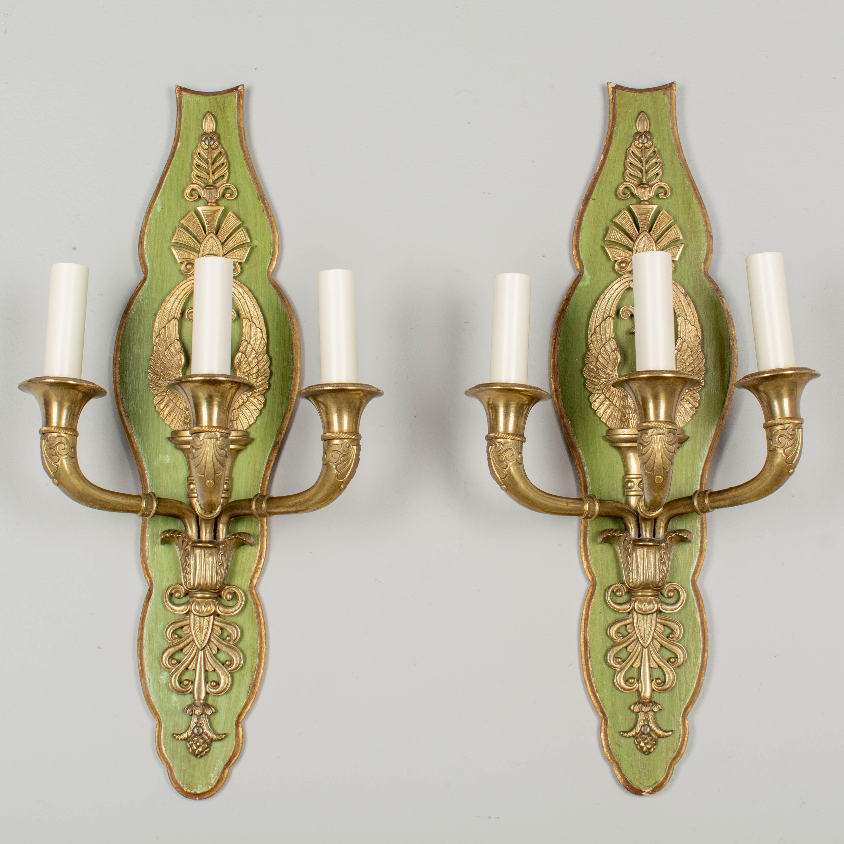 A pair of French Empire style bronze three light sconces. Fine cast details including a swan with three dimensional neck and outstretched wings. Beautiful old patina. Wood backplate with green painted finish and gilt trim. In working order with new
