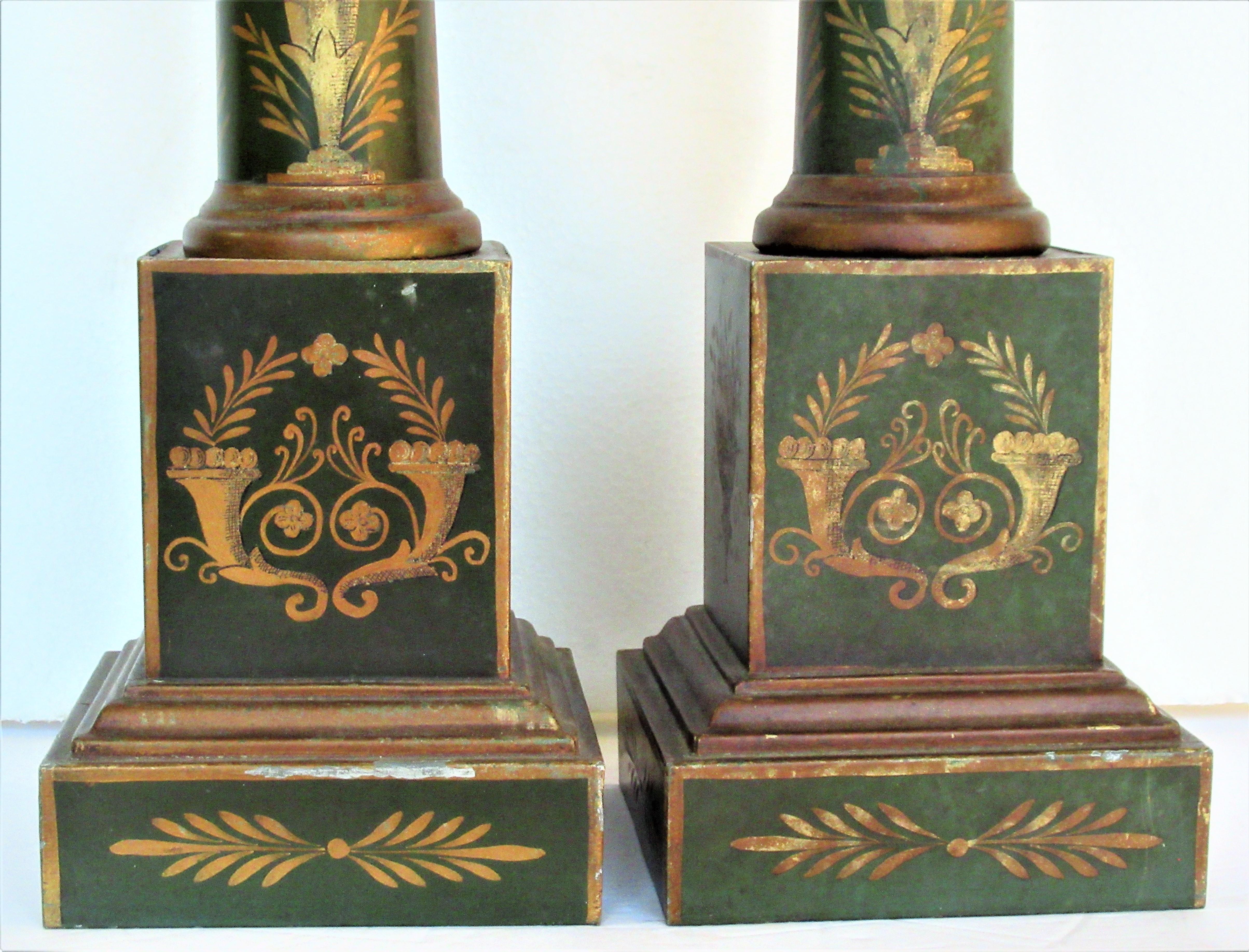 Classical French Empire style tole painted tin metal column table lamps with finely detailed gilded decoration of wreaths, baskets, cornucopia, snake handled urns, more. Great looking old lamps in overall beautifully aged original old surface color,