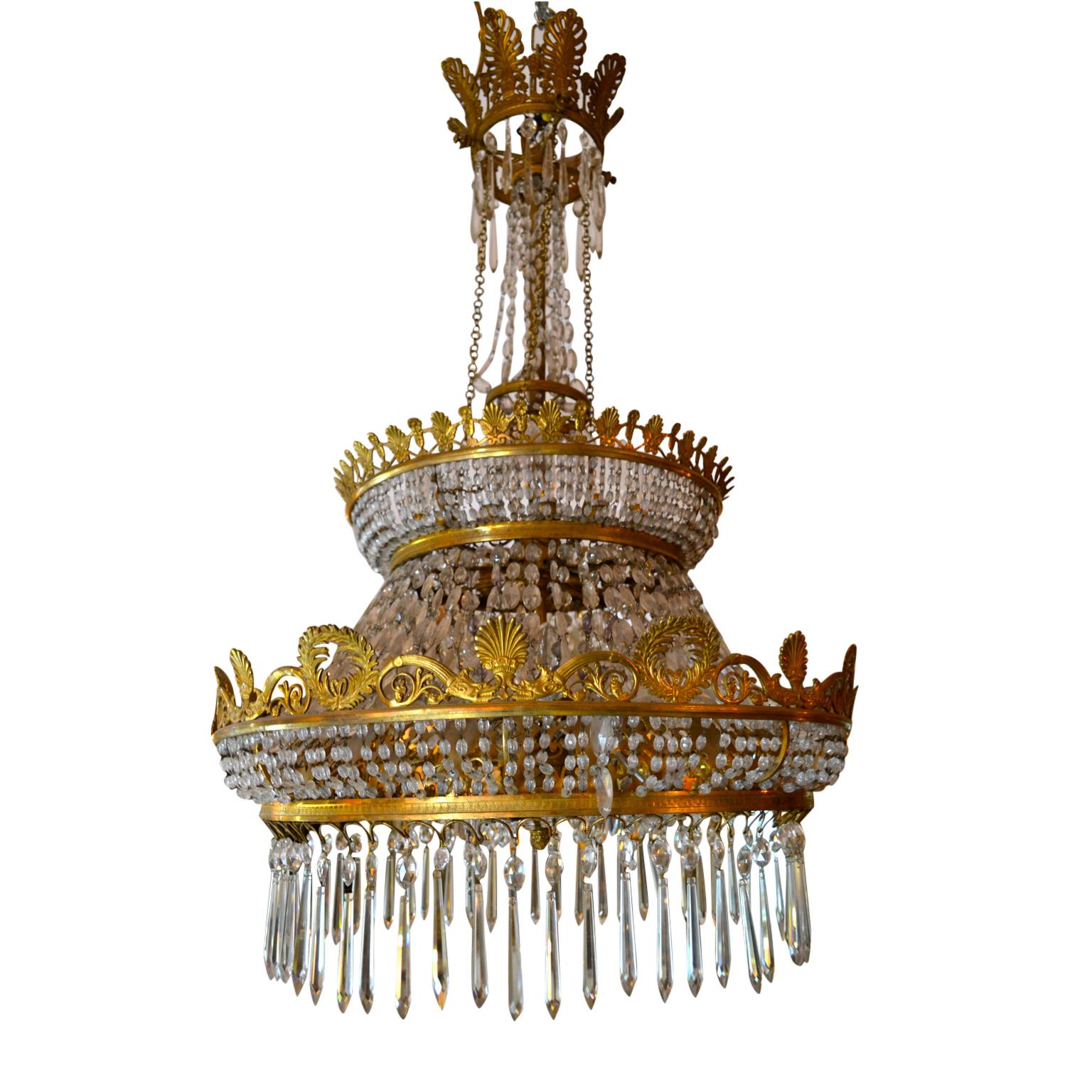 An empire style chandelier in gilded bronze and cut crystal. The large central ring is embellished with palmettes and wreaths and supports beaded chains and long crystal French drops. The underside of the ring is star shaped and woven with crystal
