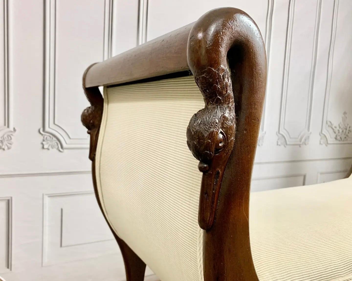 Freshly reupholstered late 19th century Empire style bench in a neutral cream-colored fabric. Artisan crafted in solid, rich walnut with elegant scrolled arms featuring hand-carved swan figureheads, supported on sleek cabriole legs finished with