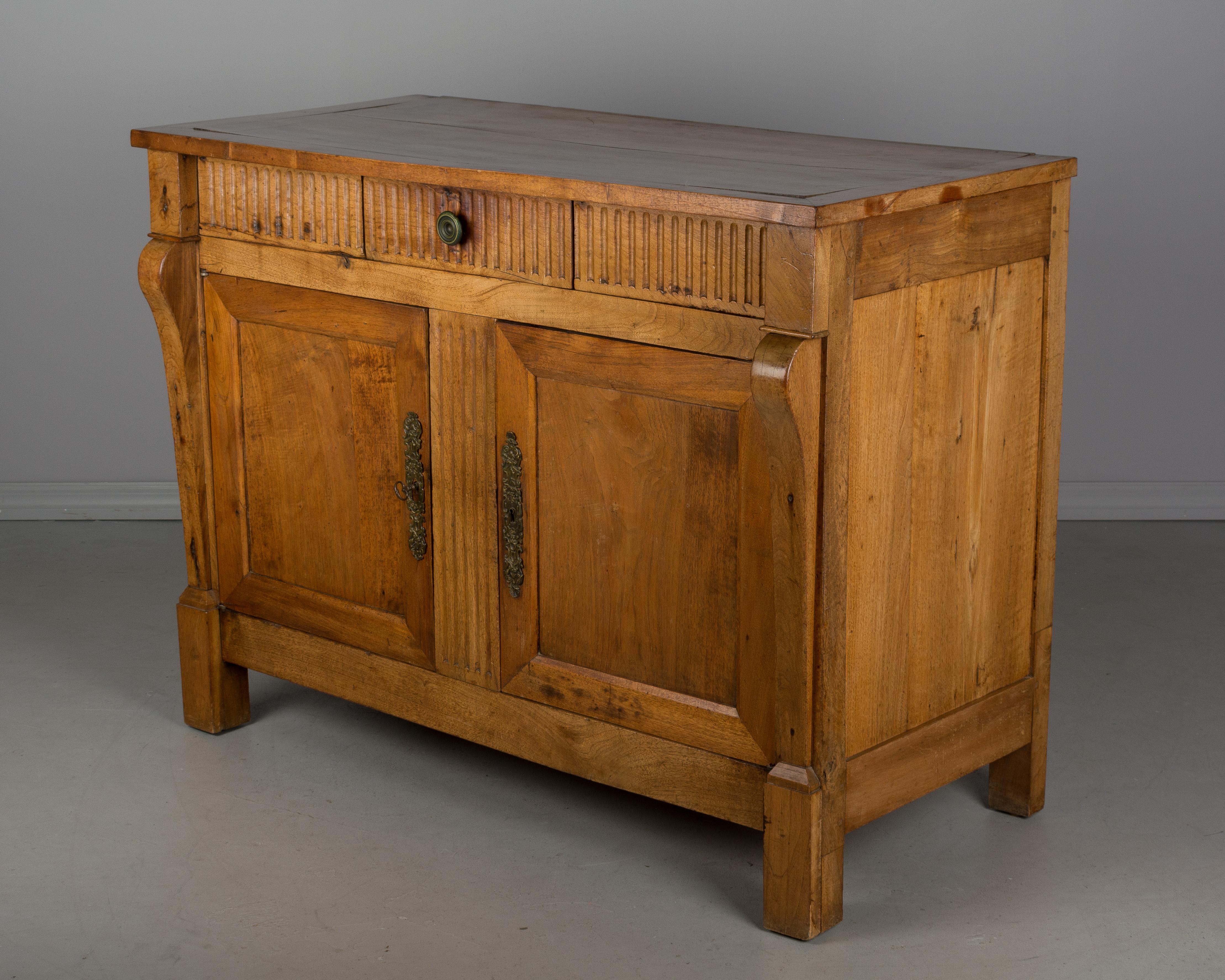 A French Empire style solid walnut buffet. Two doors with working locks and one key open to one shelf. One dovetailed drawer in the center with brass knob. Nice character to the wood. A solid sideboard in good restored condition.