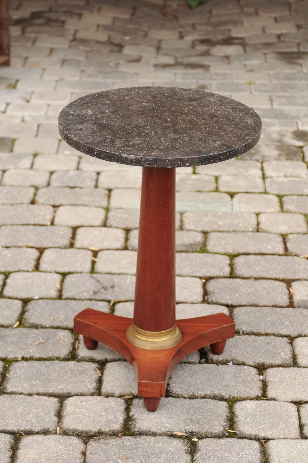 A French Empire style walnut gueridon table with grey flecked marble top and pedestal base with bronze mount from the second half of the 19th century. This French Empire style table features a circular dark grey flecked marble top, raised on a
