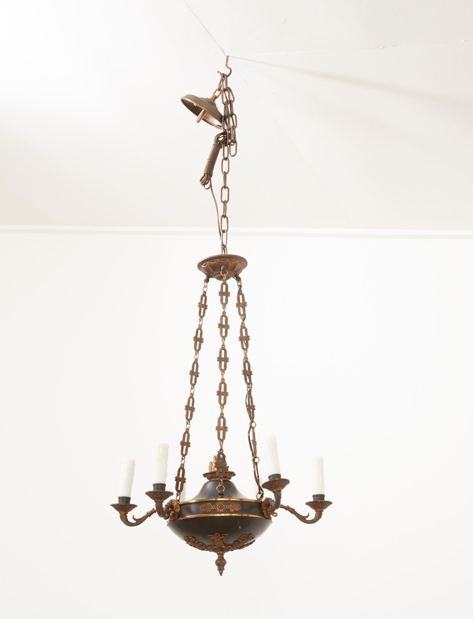 This Empirically styled six arm chandelier is just as artful as it is functional. Black tole and patinated brass contrast each other wonderfully. The underside of the bowl features stylized floral ormolu and a decorative final. The arms protrude