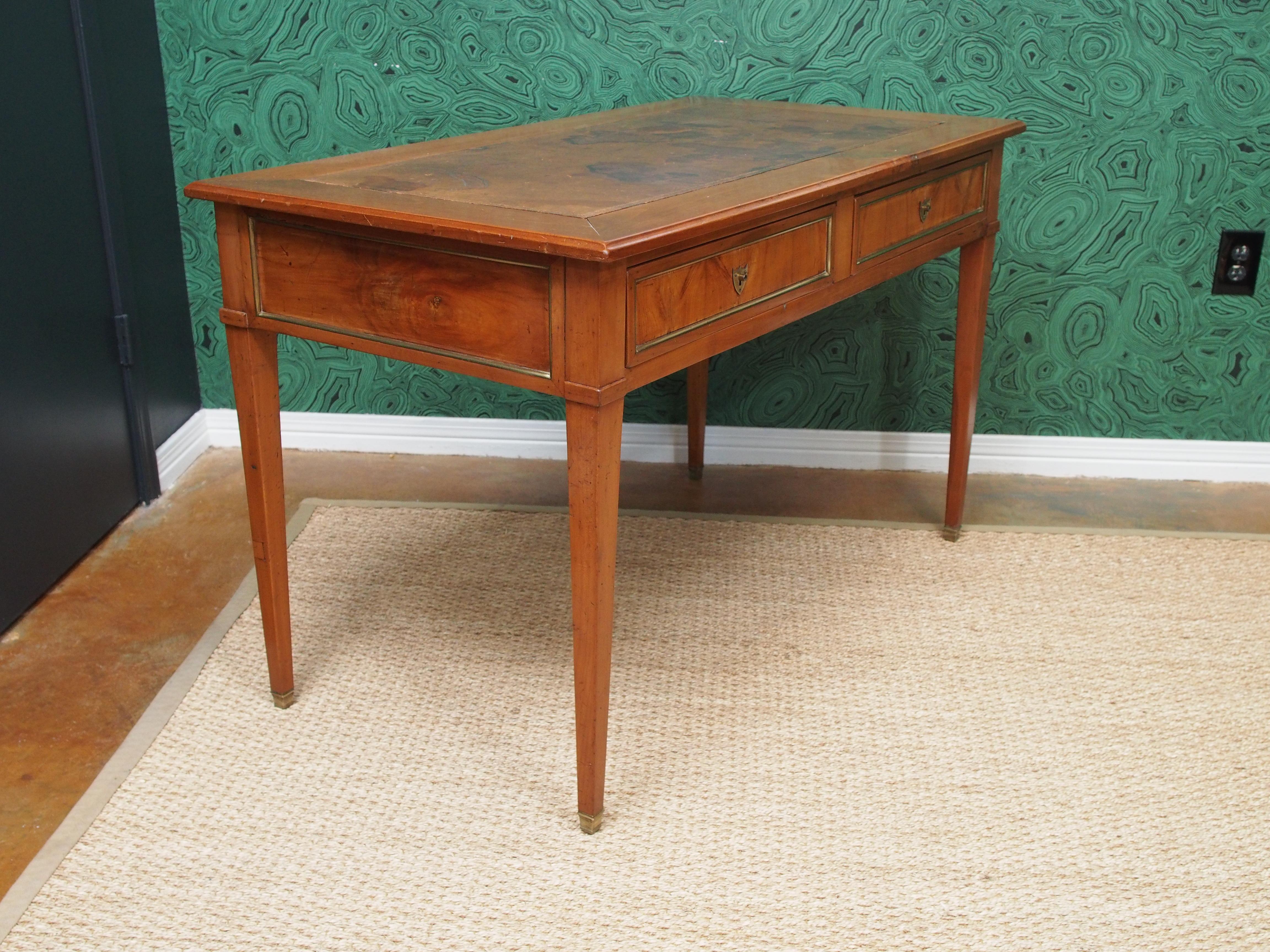 French Empire walnut writing table with tapered legs, brass trim, and original leather top.