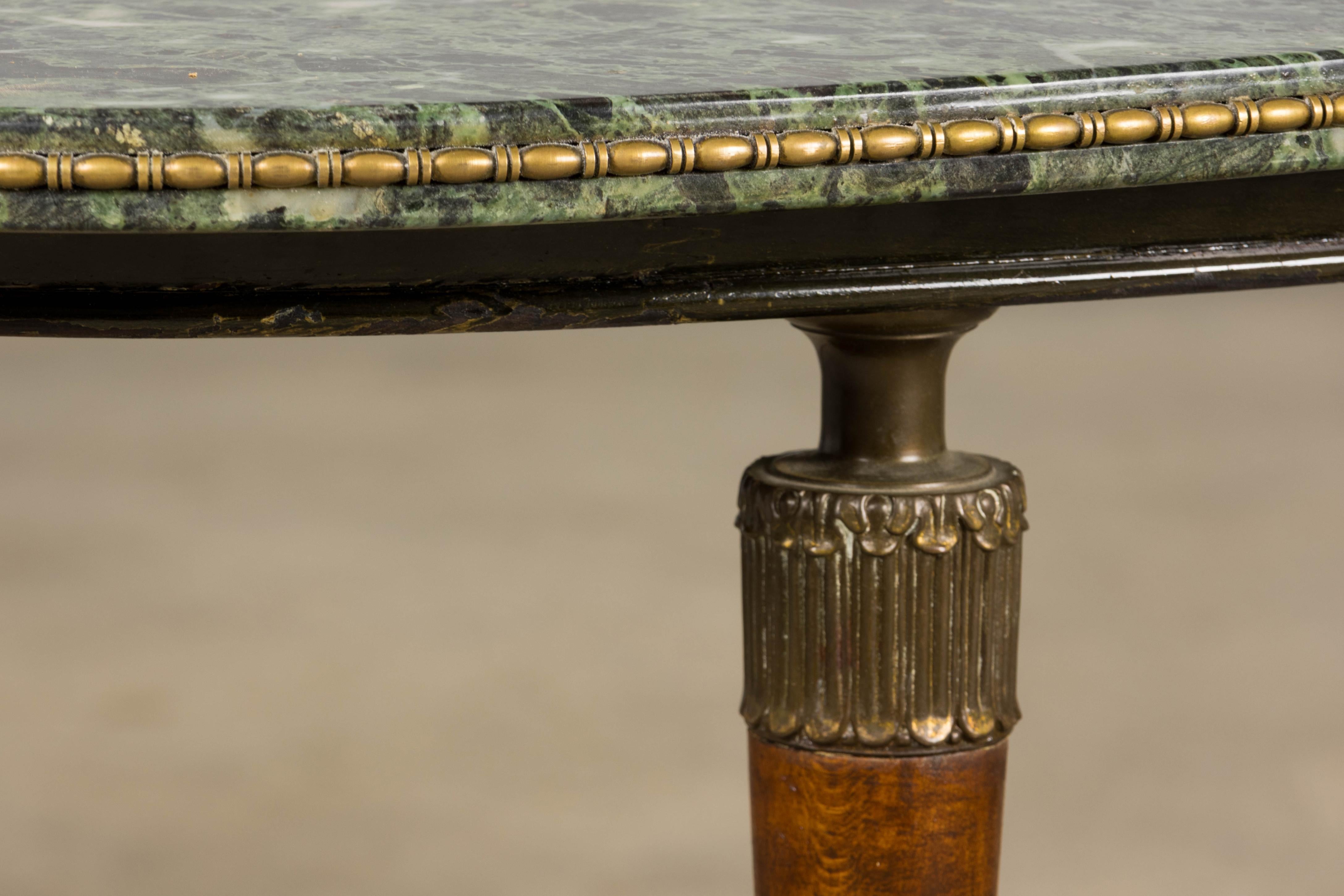 Exquise table basse de style Empire français du milieu du XXe siècle, provenant de Provence. La pièce présente un gracieux plateau ovale en marbre italien vert foncé avec des veines blanches frappantes, bordé d'une garniture décorative en laiton.