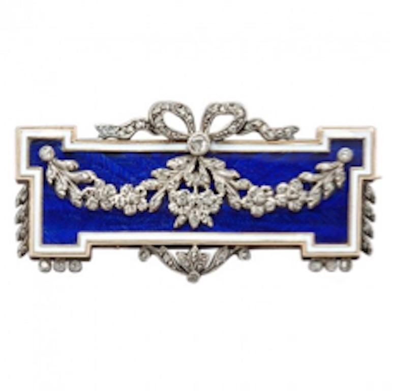 Of neoclassical design, this beautiful Parisian 18k gold pin is decorated with translucent cobalt blue enamel over an etched herringbone ground, applied with a ribbon-tied rose diamond floral garland within a white enamel border edged in diamonds.