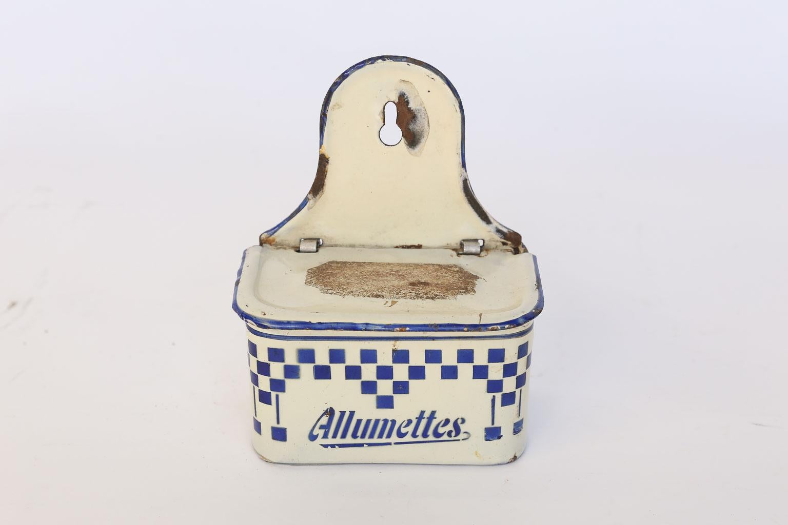 This is an antique French enamel match holder and striker made in the early 1900s. This piece can be wall-mounted or sit alone on a counter or tabletop. The lid has a strike patch on the top for lighting matches and lifts to reveal the stored