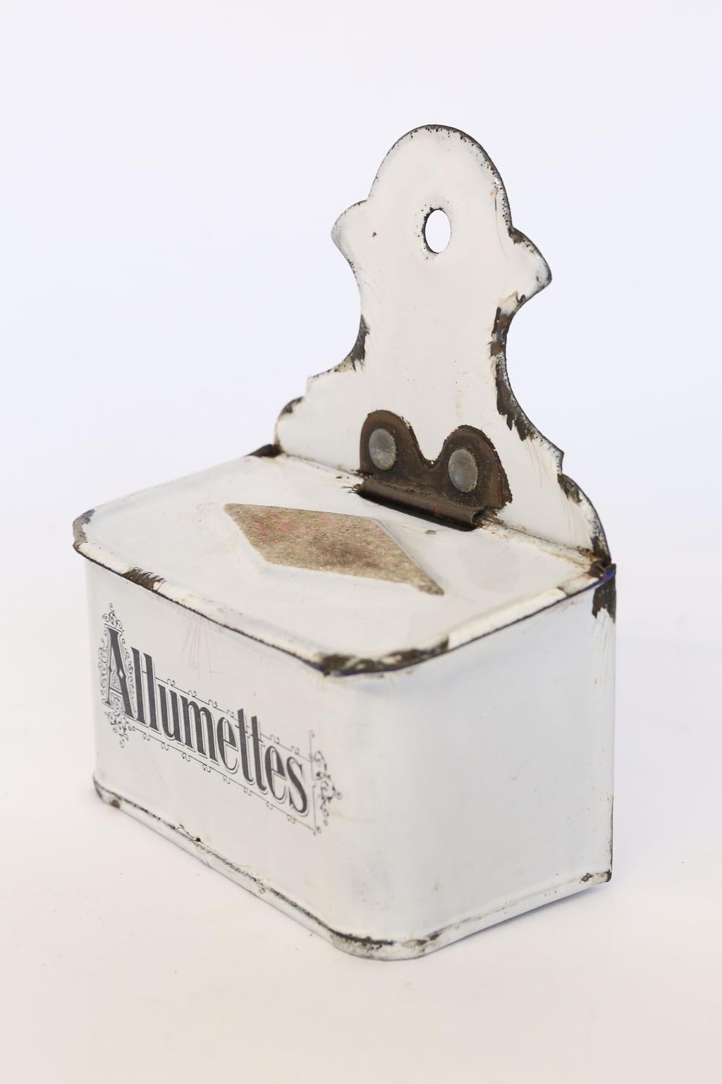 This is an antique French enamel match holder and striker made in the early 1900s. This piece can be wall-mounted or sit alone on a counter or tabletop. The lid has a strike patch on the top for lighting matches and lifts to reveal the stored