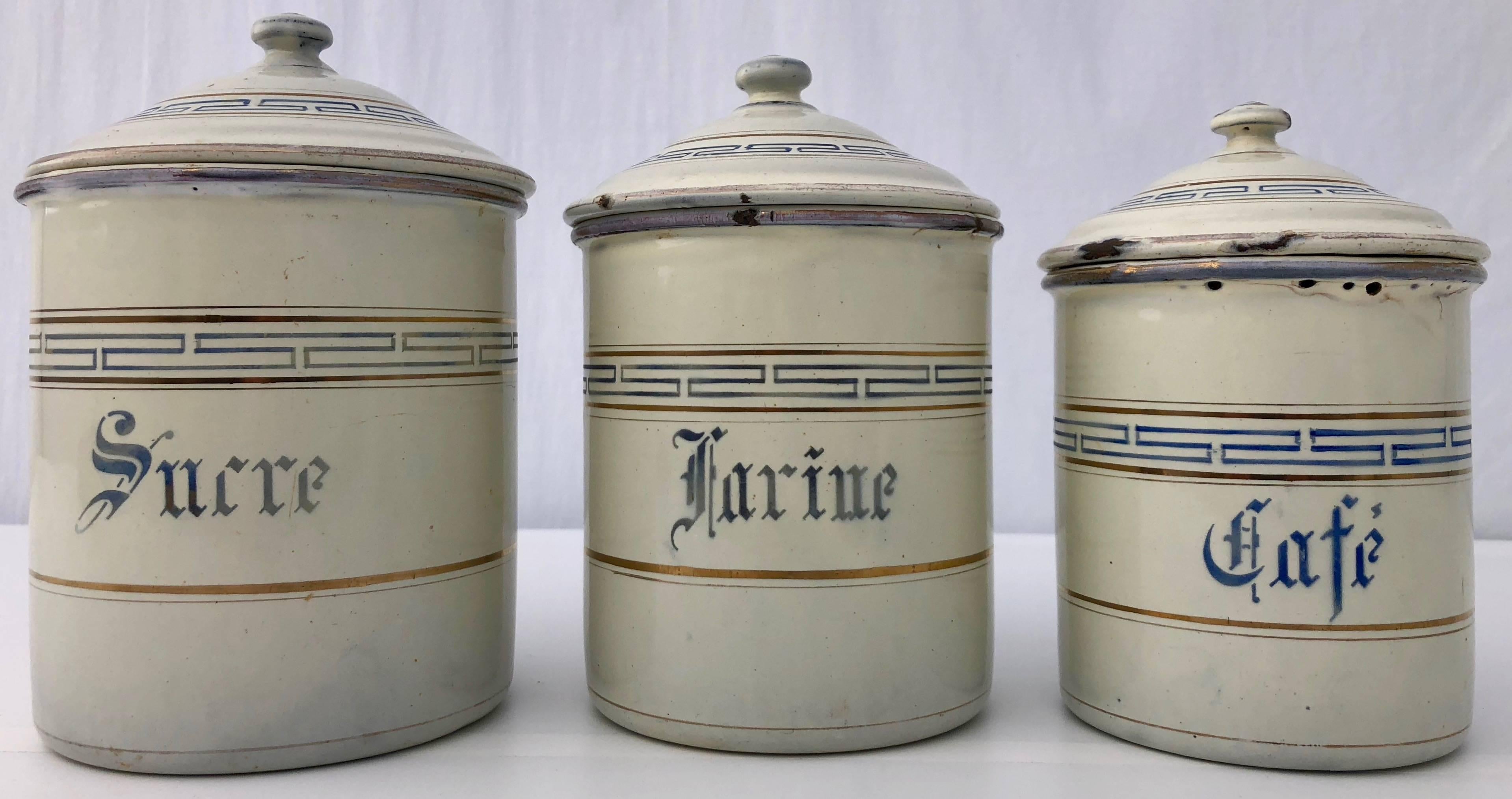 This French enamelware canister set includes six graduating sizes of jars with their matching lids. They are in a beautiful off white color with blue and gold trim and blue French lettering indicating their original use. The jars nest in each other