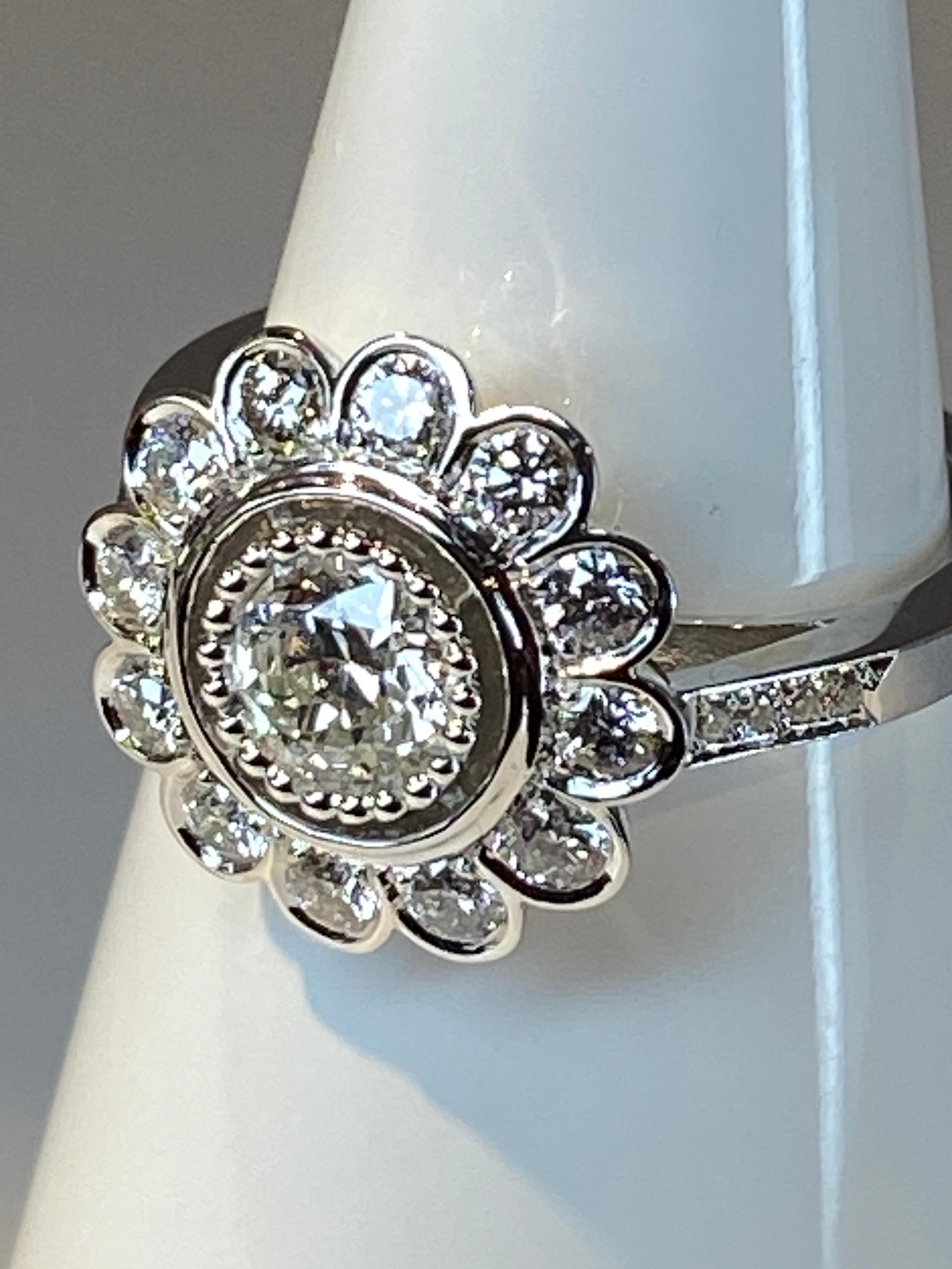 Ravissante bague en or 18 carat de modèle fleur «marguerite»ornée au centre d’un diamant de taille brillant pesant 0.48 carat entouré de 12 diamants de taille brillant pesant 0.54 carat. Le diamant central est en serti perlé et les diamants