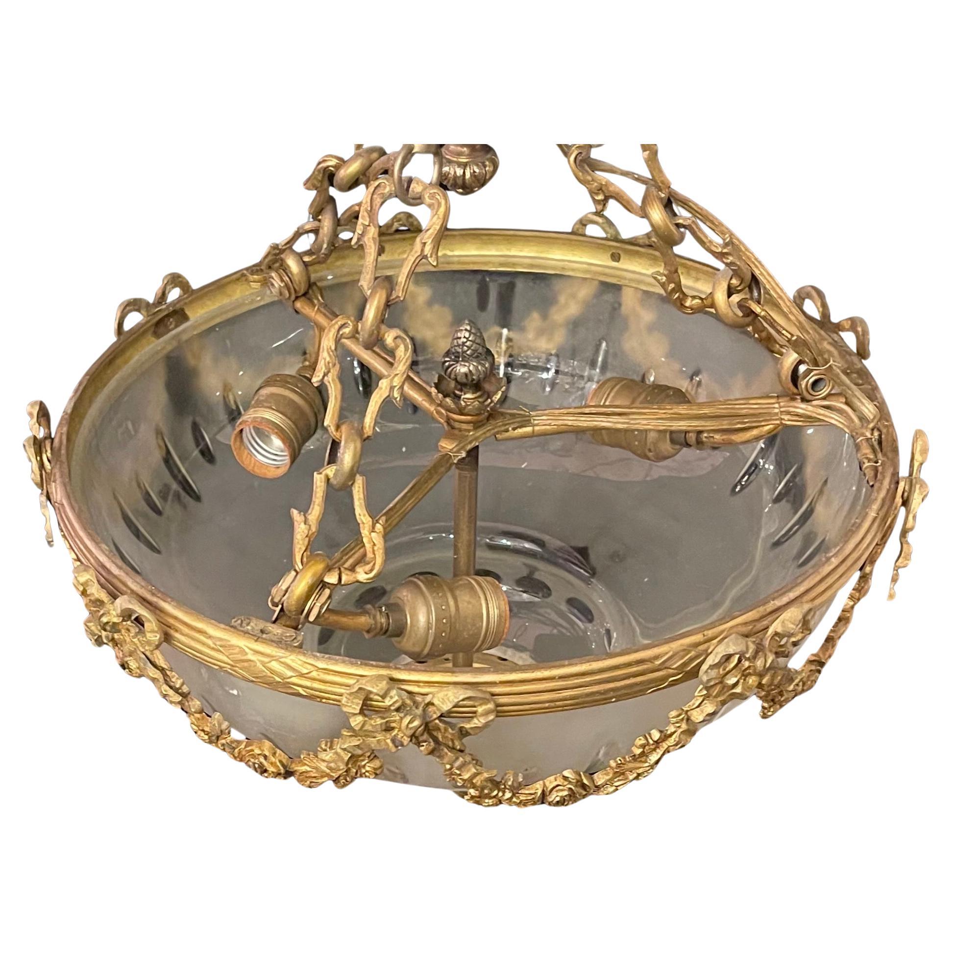 Un magnifique abat-jour en verre dépoli gravé à la française se trouve à l'intérieur d'un boîtier en bronze doré avec des guirlandes et des nœuds dans le style Louis XV. Ce lustre a 3 douilles Edison et le luminaire est livré prêt à être installé