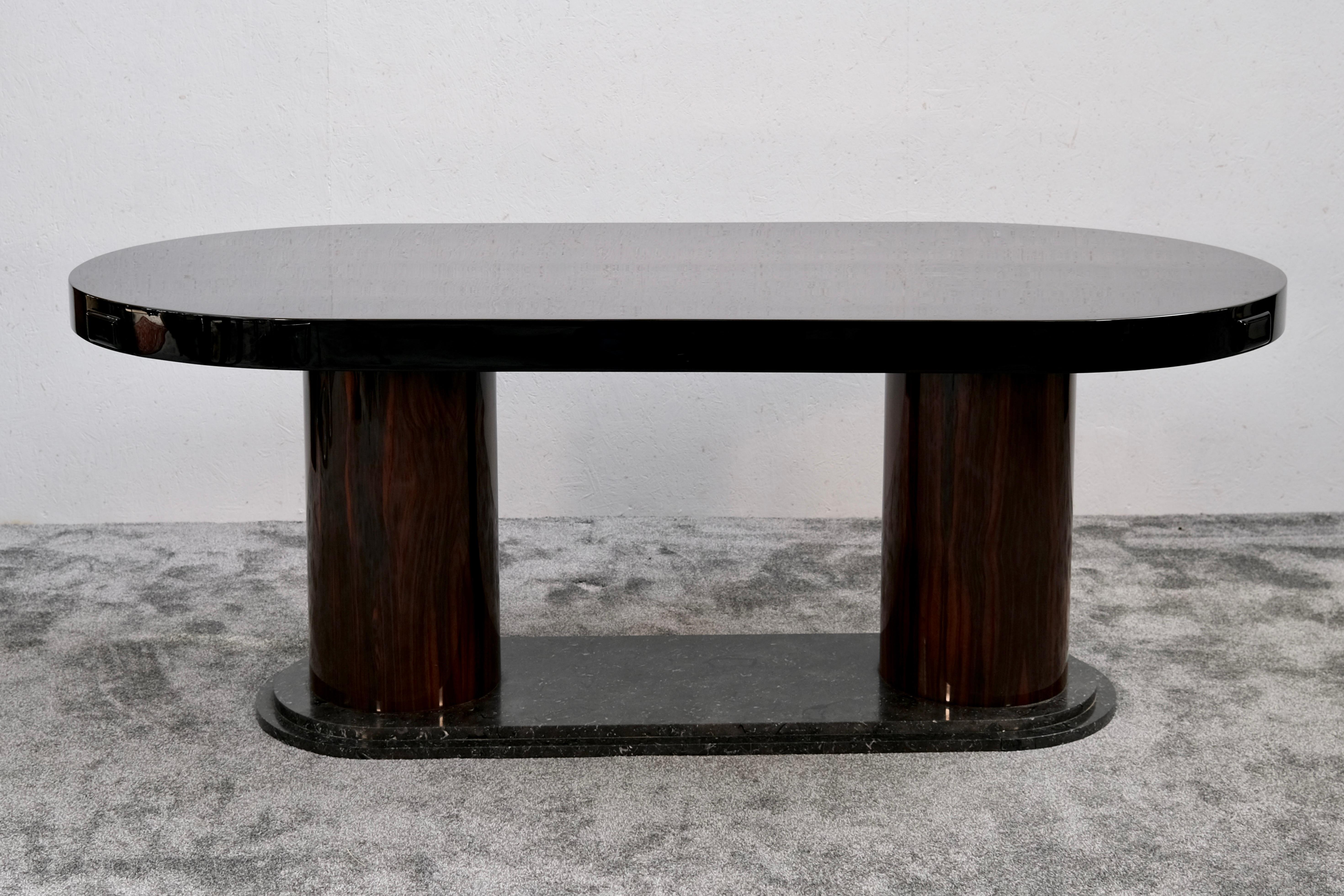 Esta mesa de comedor, un sorprendente ejemplo del diseño Art Déco francés de los años 30, muestra una mezcla perfecta de fuerza arquitectónica y refinada elegancia. Dos potentes columnas cilíndricas, chapadas en madera exótica (Macassar), están