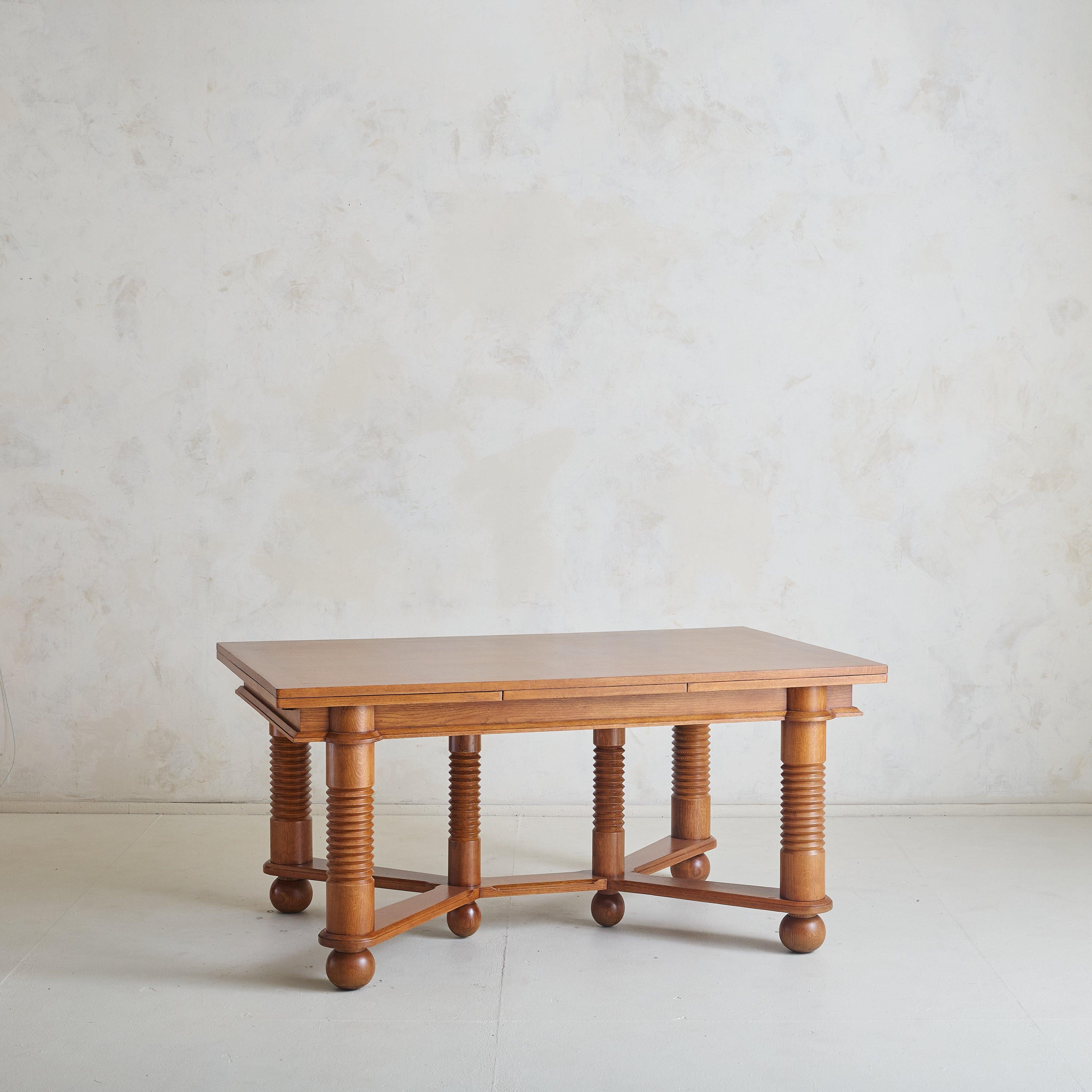 A 1940s extendable oak dining table attributed to French designer Charles Dudouyt. The table showcases Dudouyt’s signature architectural geometry, with bold turned legs that stand grounded on ball feet. Its sculptural base adds a rhythmic texture,