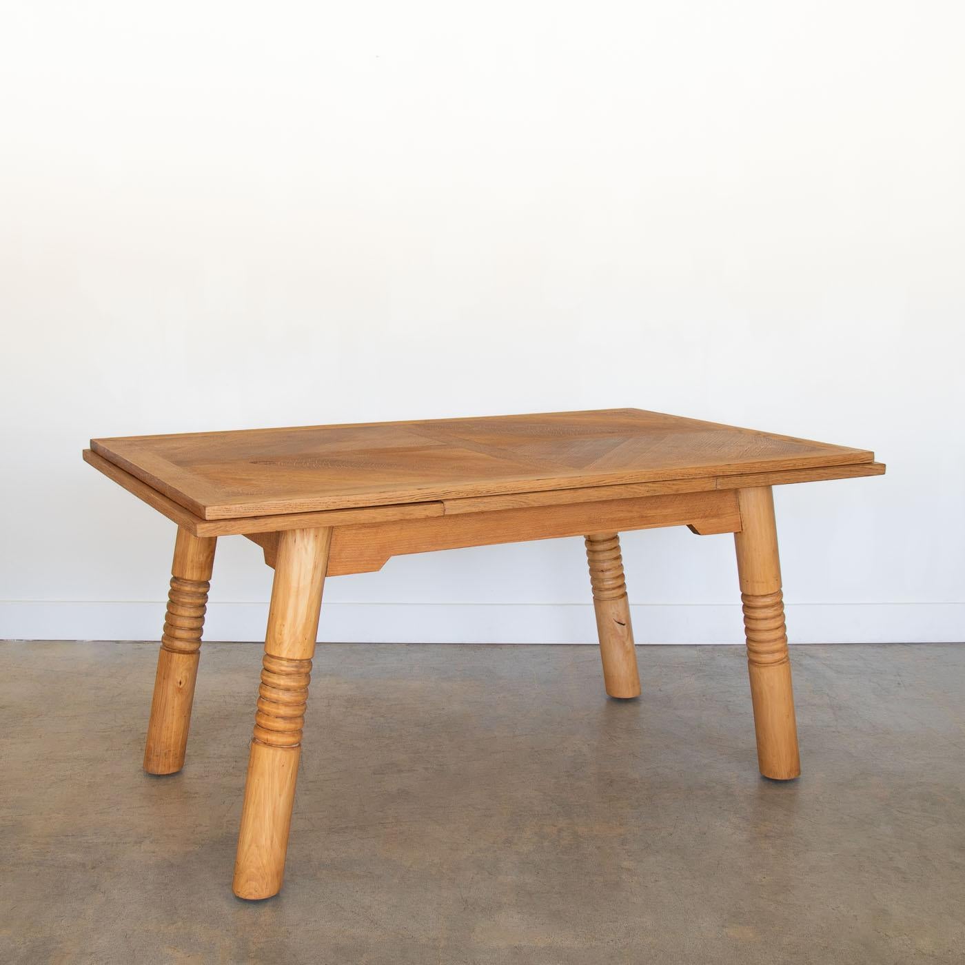 Incroyable table de salle à manger extensible en bois de Charles Dudouyt, France, années 1940. Superbe plateau rectangulaire en bois de chêne avec un design de parquet et deux panneaux coulissants de chaque côté. La base est en bois d'érable et